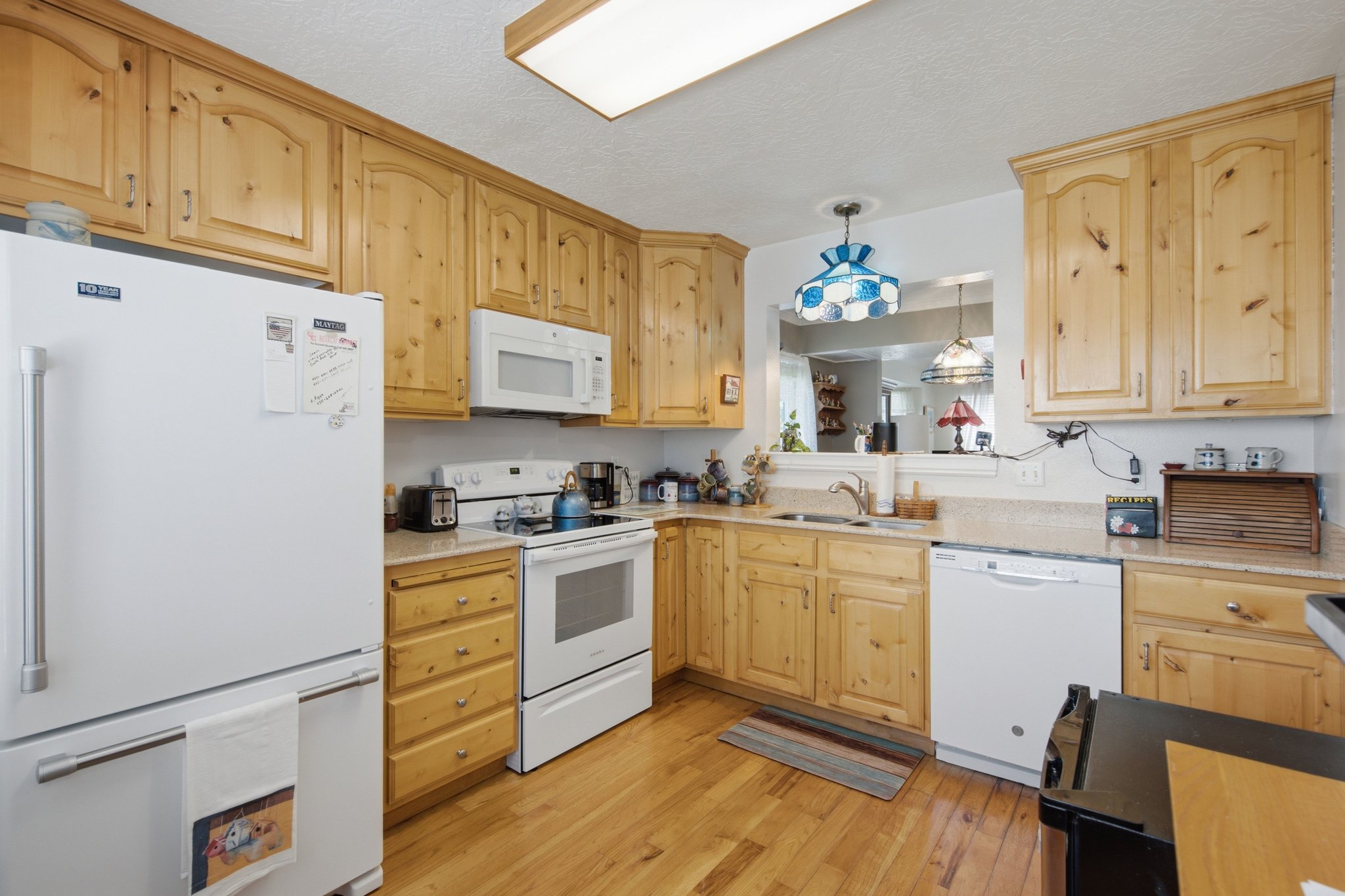 Kitchen featuring light wood cabinetry, light wood-finish flooring, white appliances, a pass-through window, and a recessed ceiling light