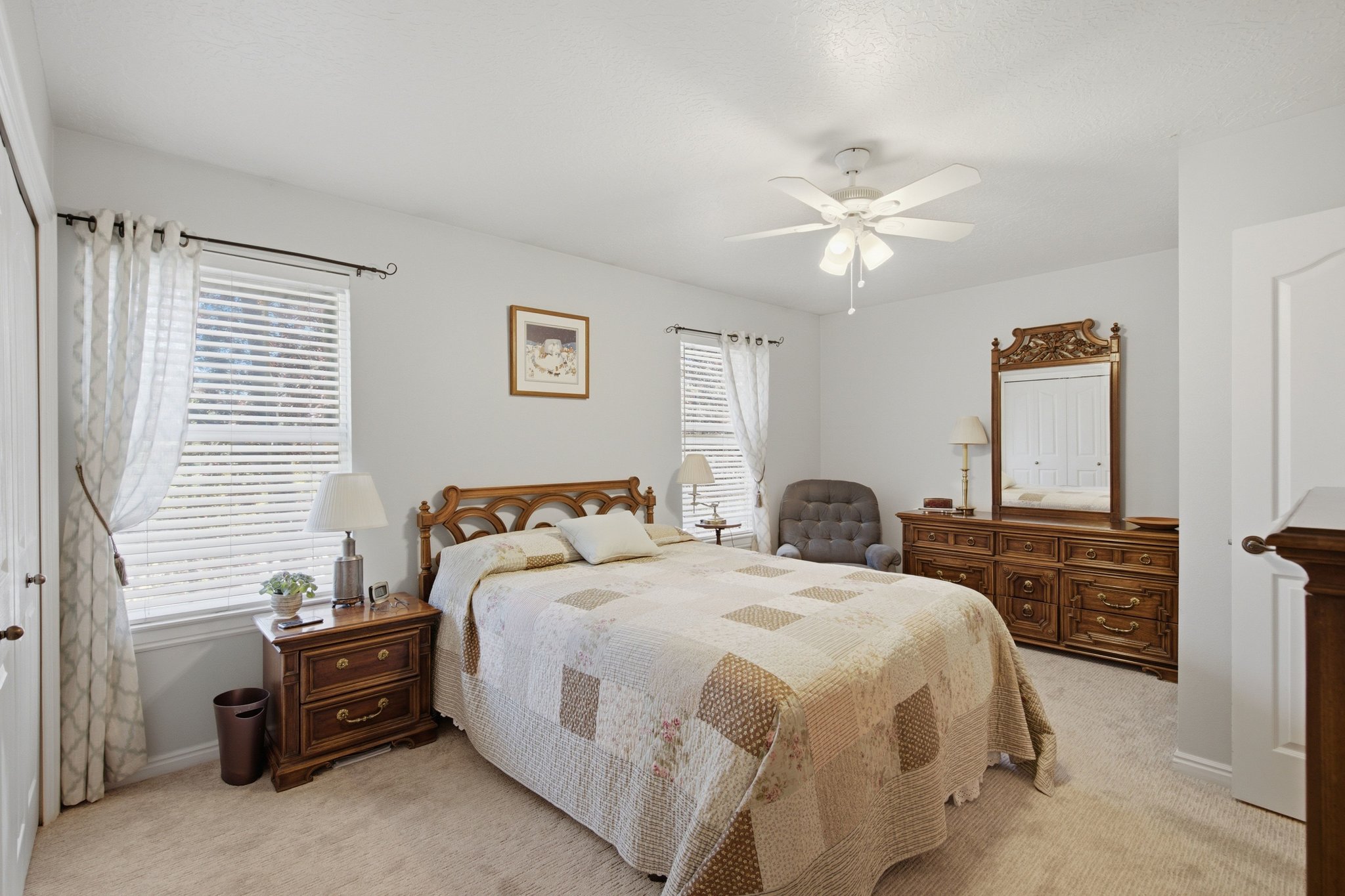 Carpeted bedroom with two windows featuring blinds and drapes
