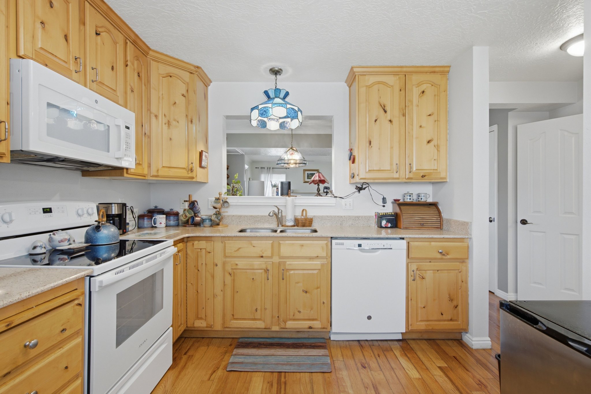 Kitchen featuring wood-finish flooring, wood cabinetry, stone-look countertops, and white appliances including a microwave, range, and dishwasher