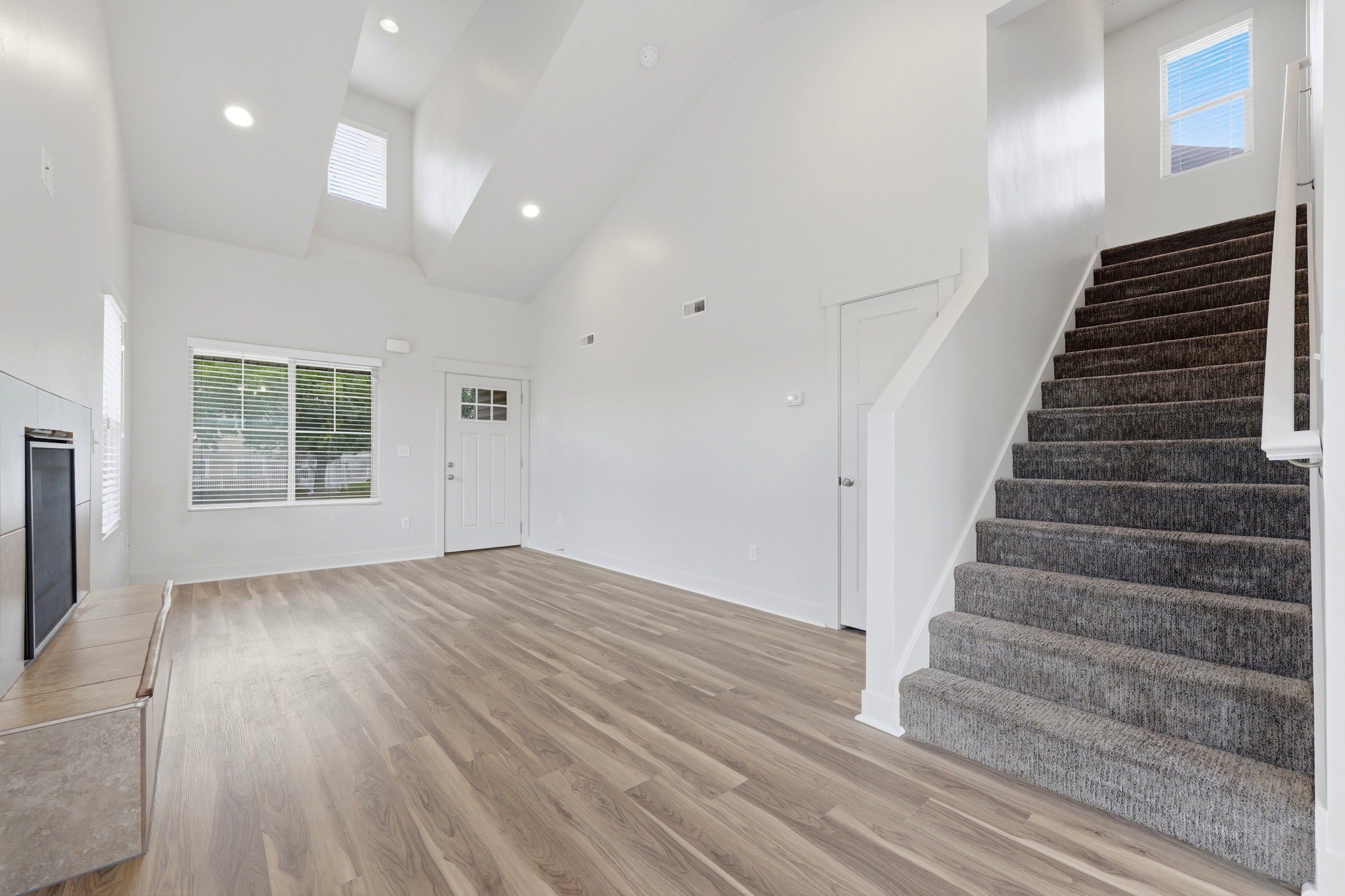Spacious living area featuring vaulted ceilings, wood-finish flooring, a built-in fireplace, and abundant natural light from multiple windows