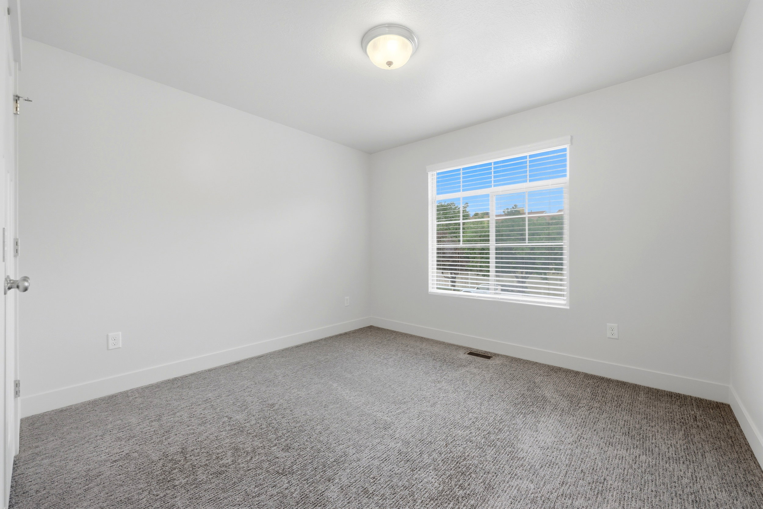 Neutral-toned room featuring a large window with horizontal blinds, carpeted flooring, white walls, and a ceiling-mounted light fixture