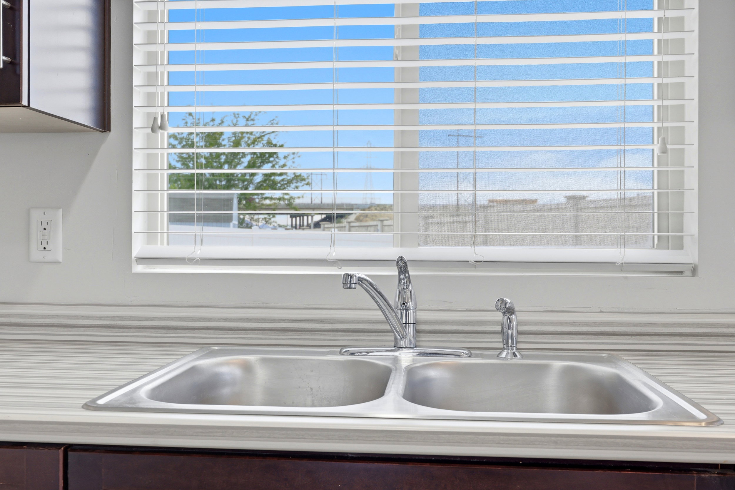 Stainless steel double basin sink with chrome faucet and spray attachment, set within a striped countertop