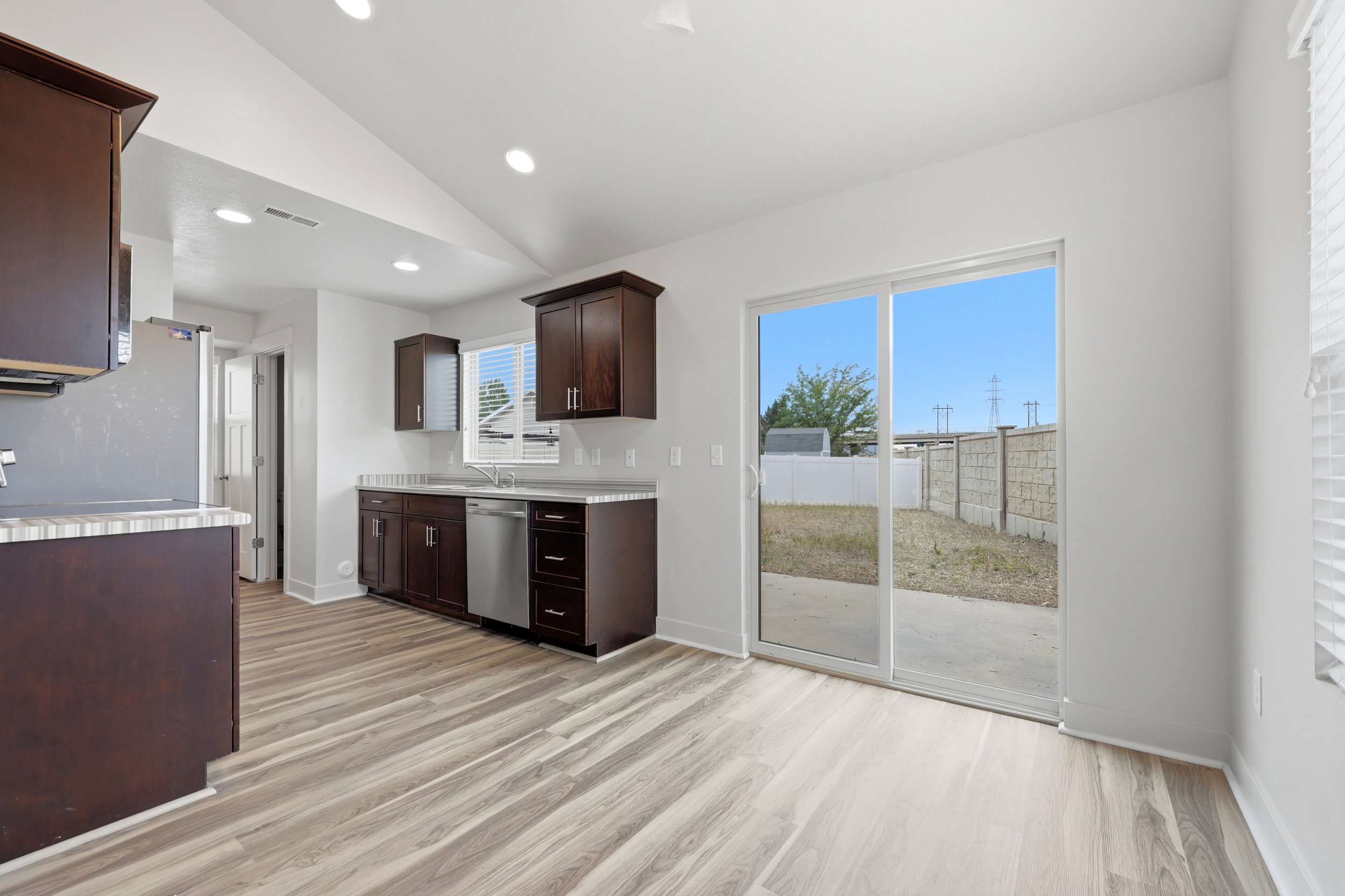 Open-concept kitchen with dark wood cabinetry, stainless steel appliances, and light wood-finish flooring