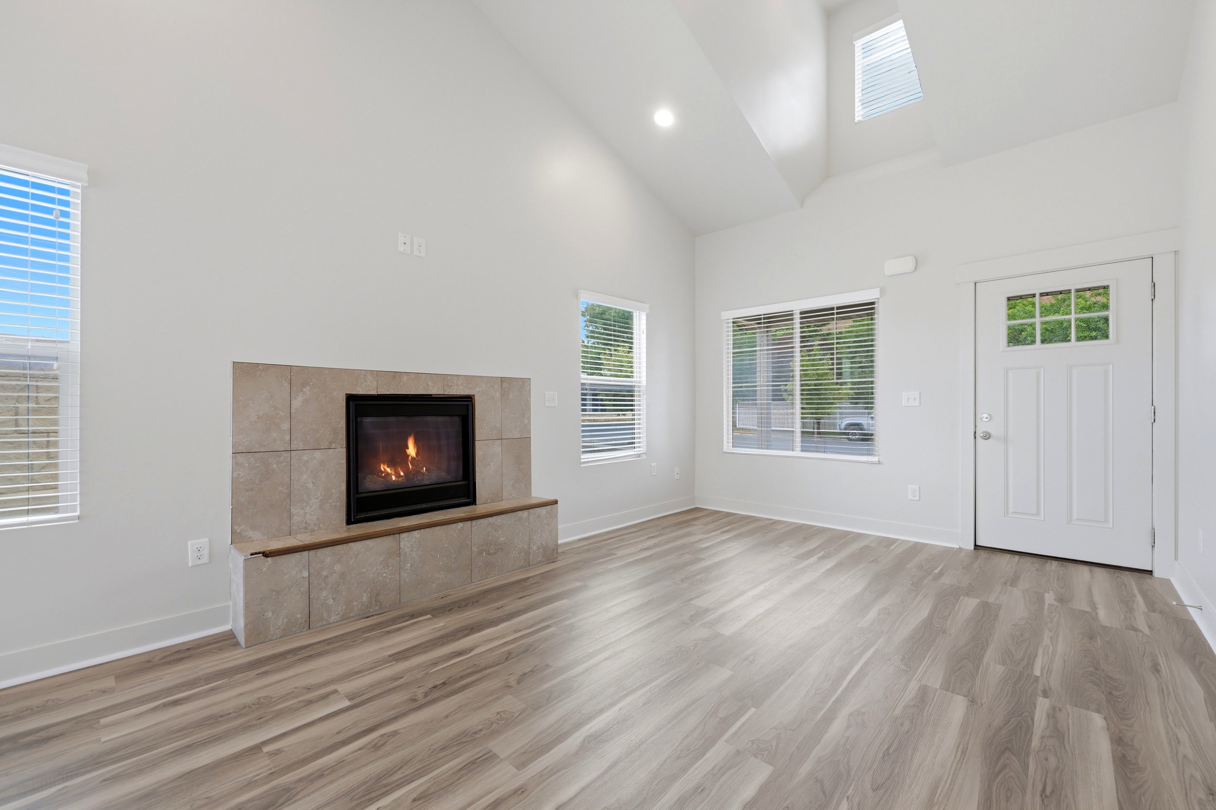 Spacious living area featuring a tile-surround fireplace, wood-finish flooring, vaulted ceilings, and skylight