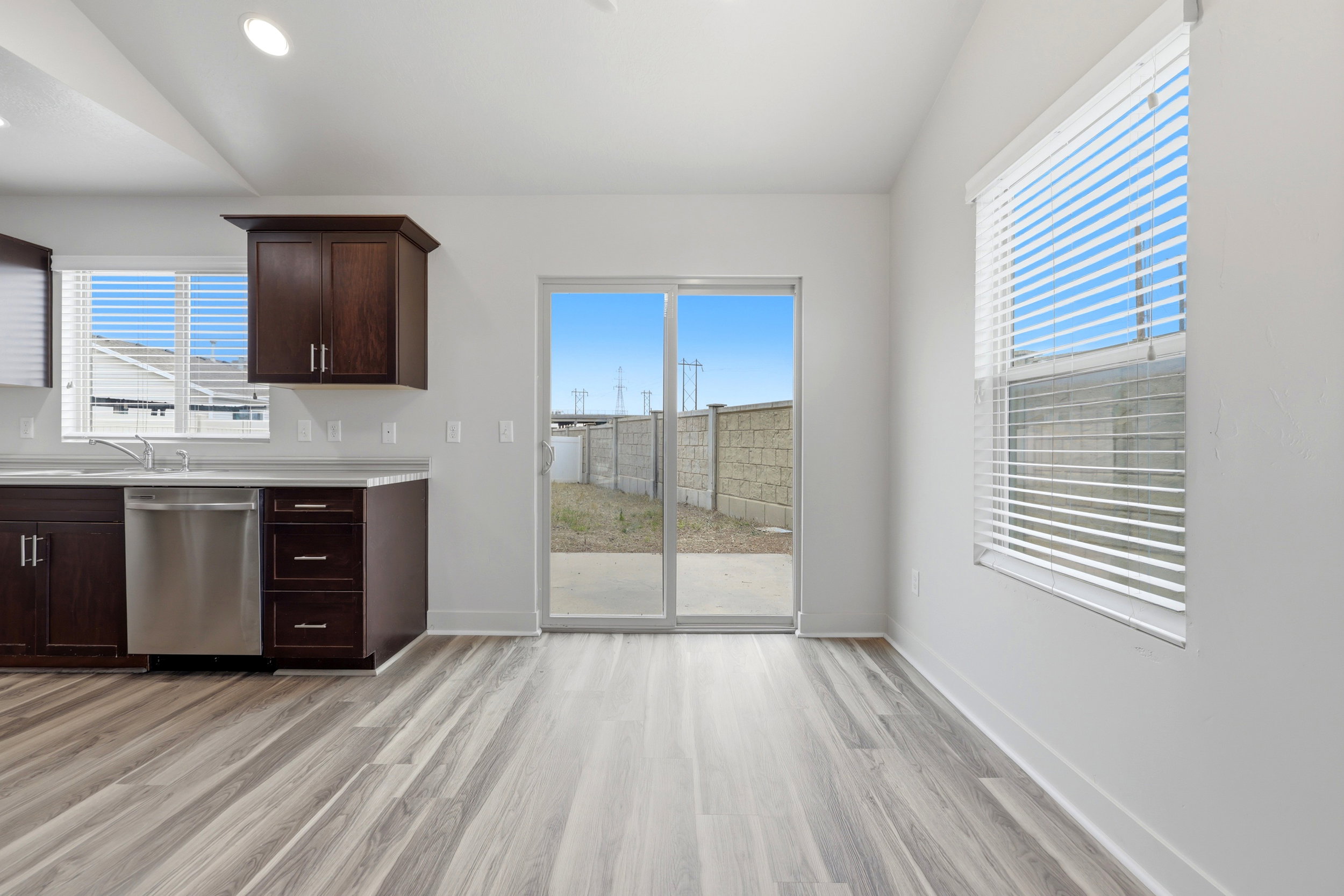 Open-concept living area with wood-finish flooring, a contemporary kitchen featuring stainless steel appliances and dark wood cabinetry, recessed ceiling lighting, and natural light from a sliding glass door and window