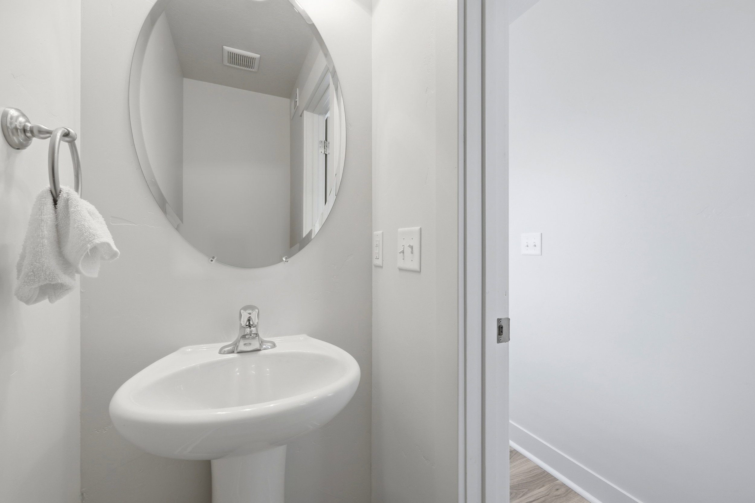 Pedestal sink with chrome faucet, complemented by an oval-shaped mirror