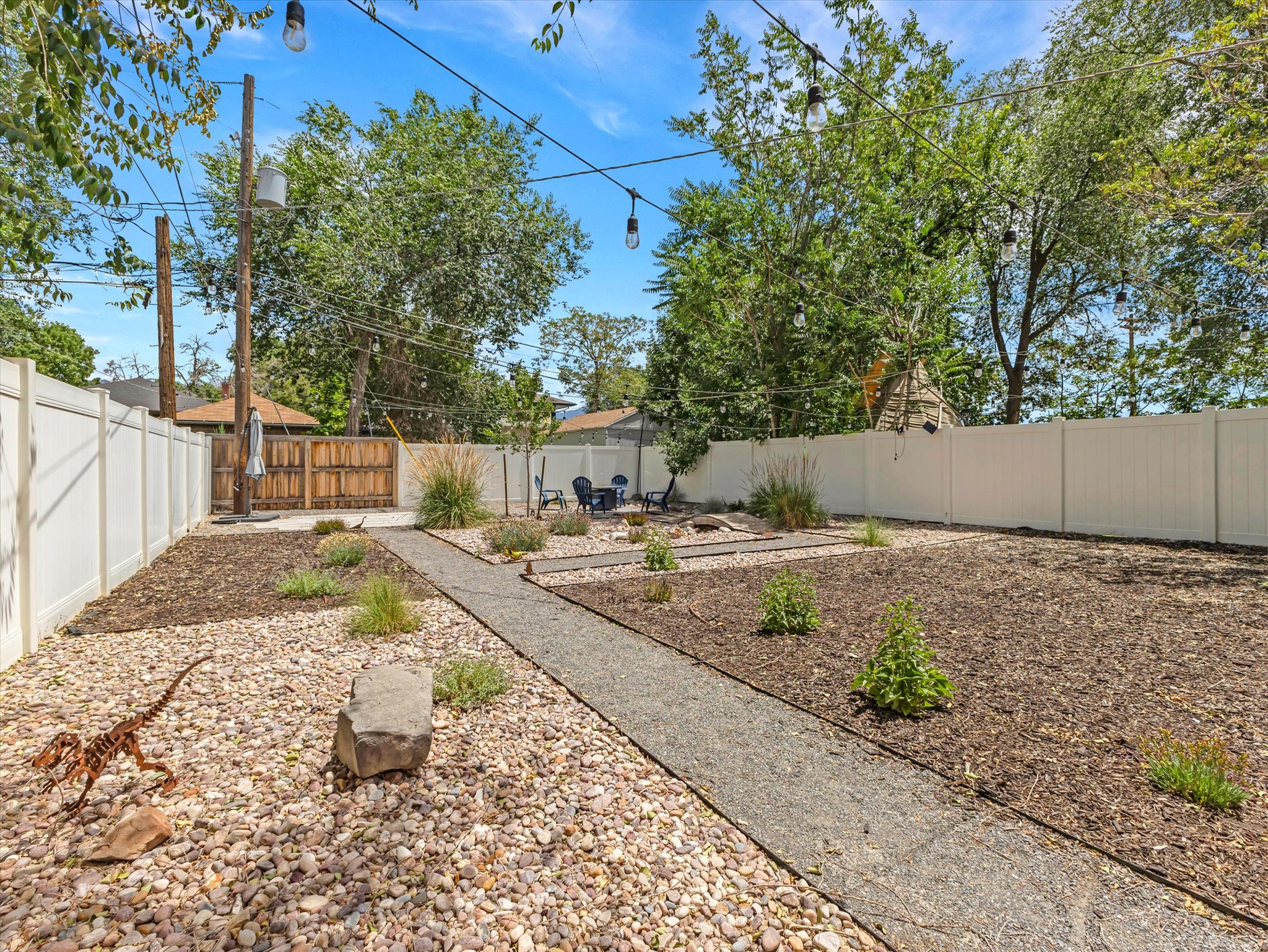 Private backyard with white vinyl fencing, a gravel pathway, and dedicated garden beds