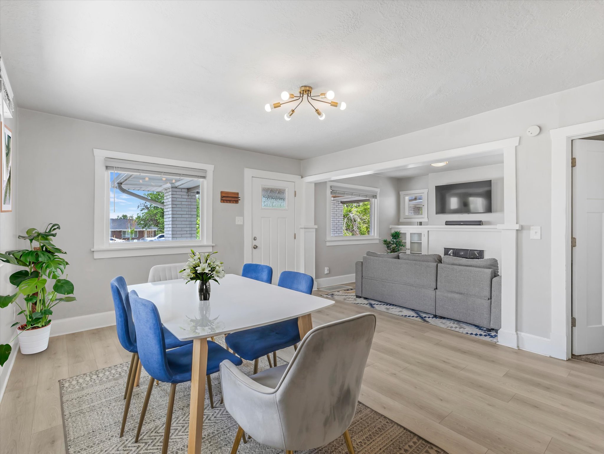 Open-concept living and dining area featuring light wood-finish flooring, a contemporary chandelier, and a bright white front door with glass inlay