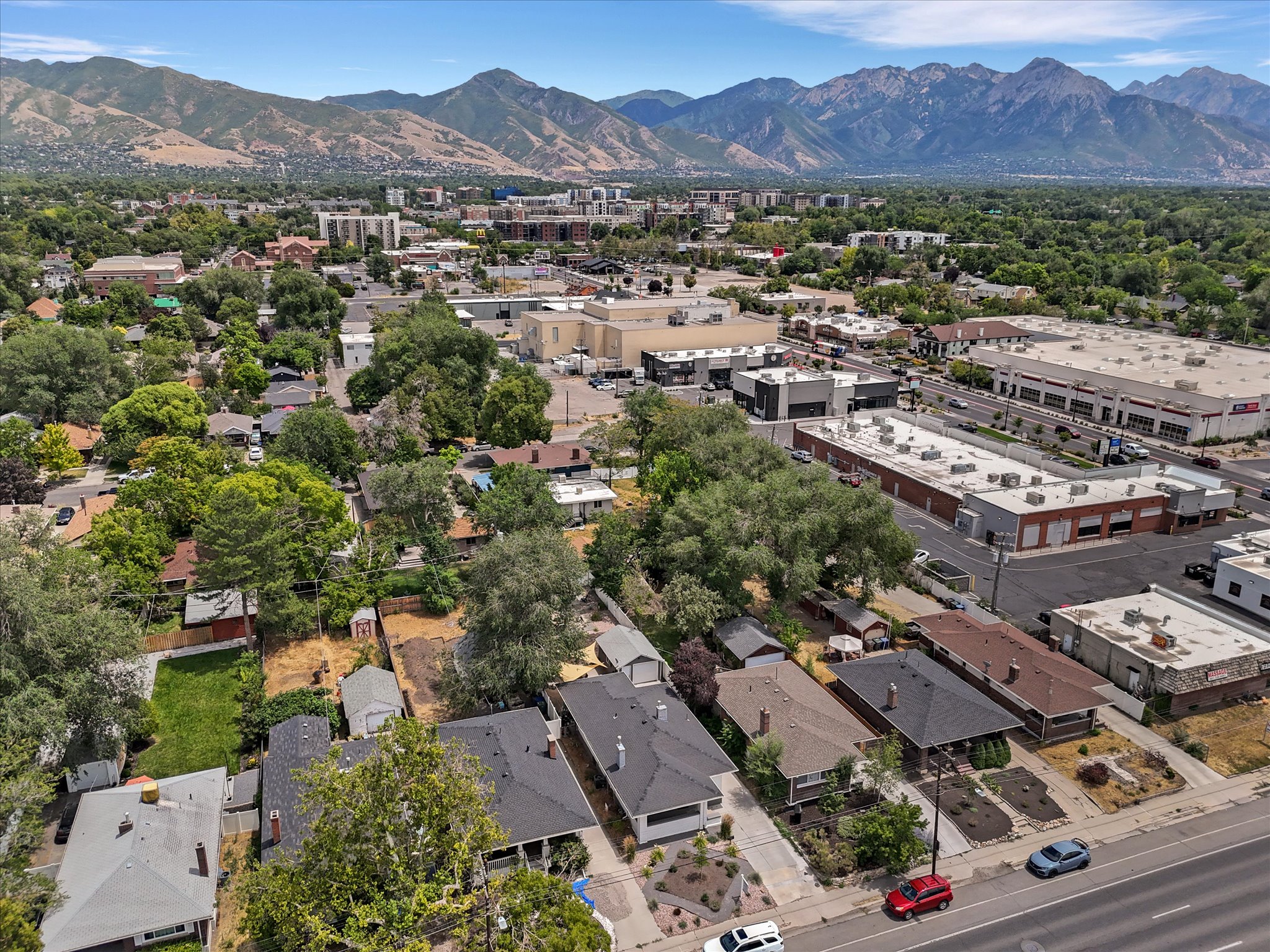 Residential area surrounded by mature trees, with commercial buildings and a mountain range in the background
