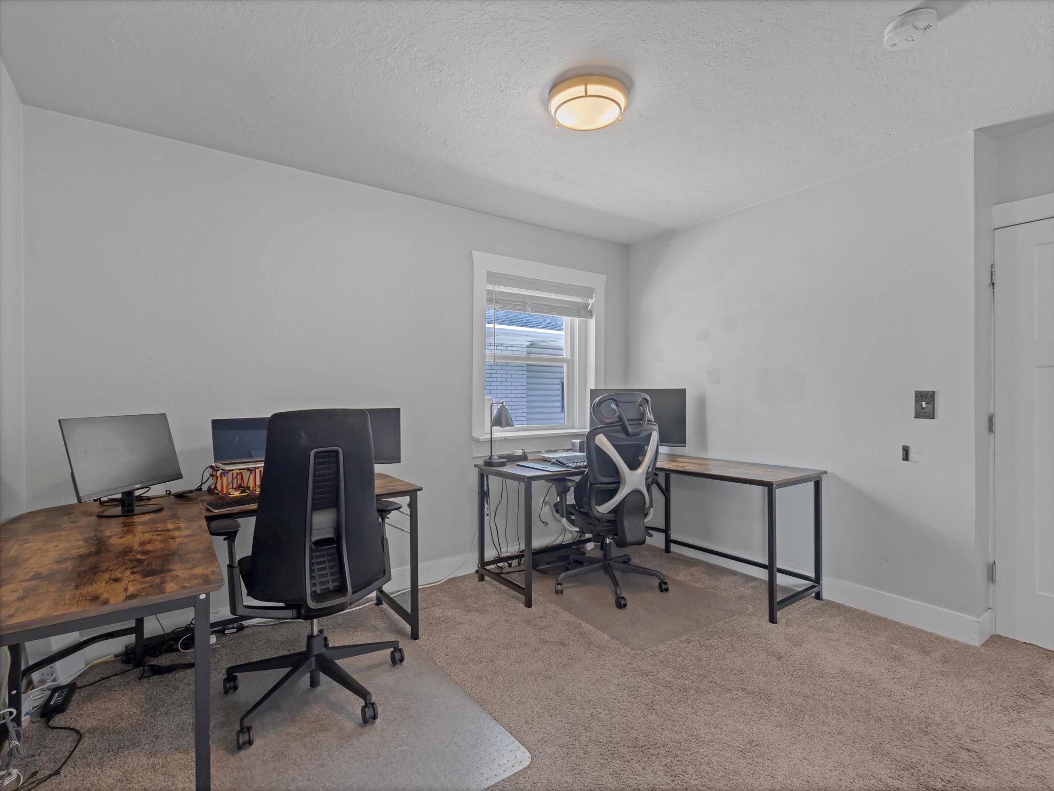 Carpeted room featuring a single window with blinds, white trim, and a flush-mount ceiling light fixture