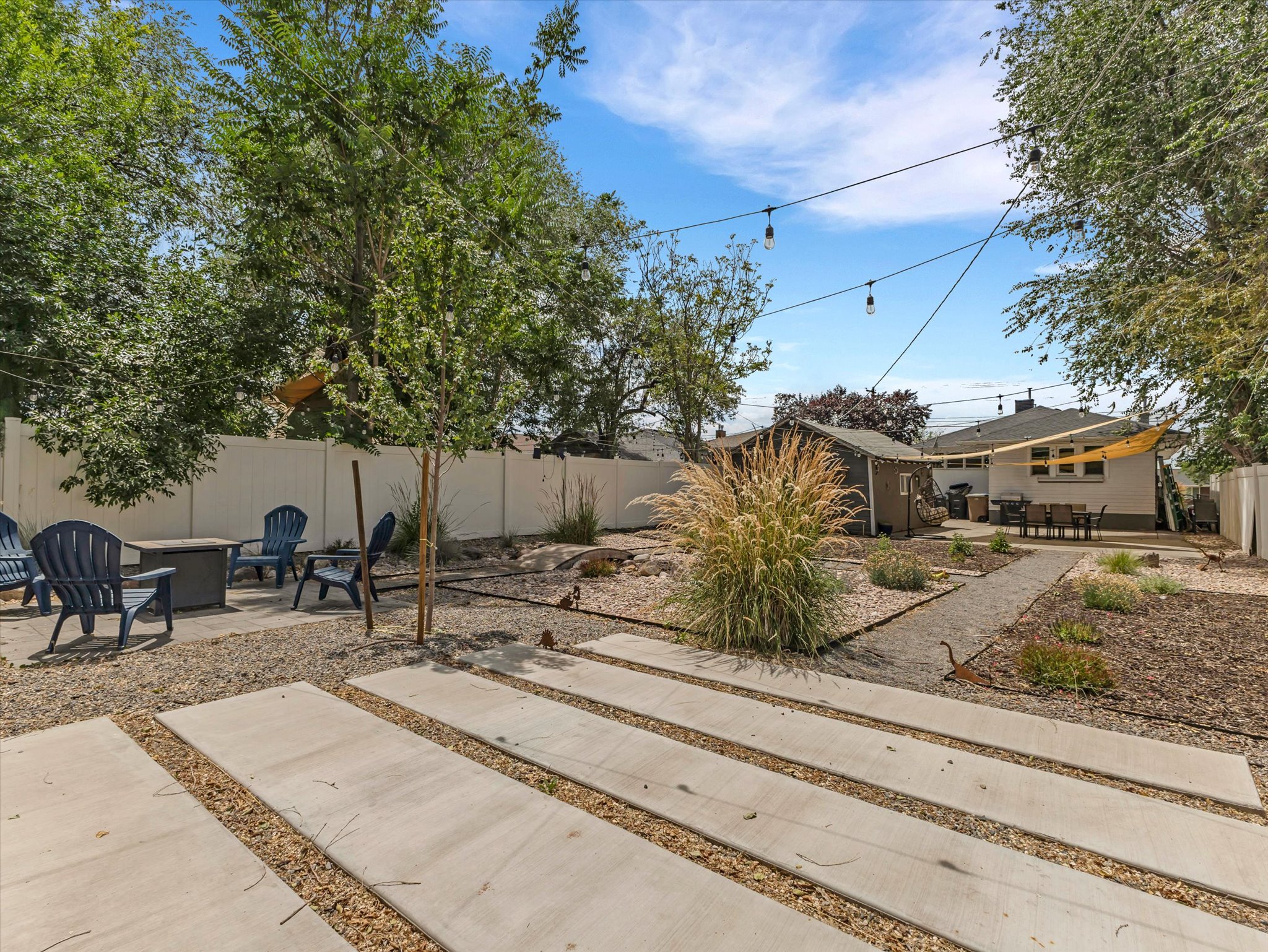 Expansive backyard featuring a concrete patio, gravel hardscaping, established trees, and string lighting