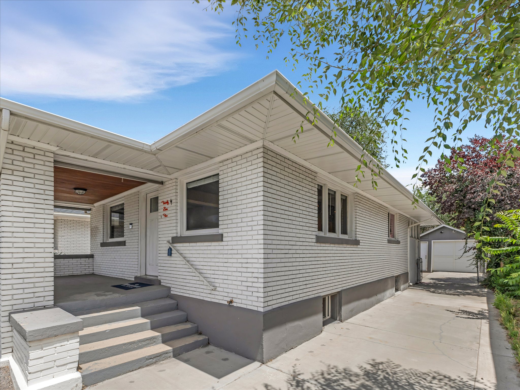 White brick exterior with a covered porch featuring a wood-panel ceiling and recessed lighting