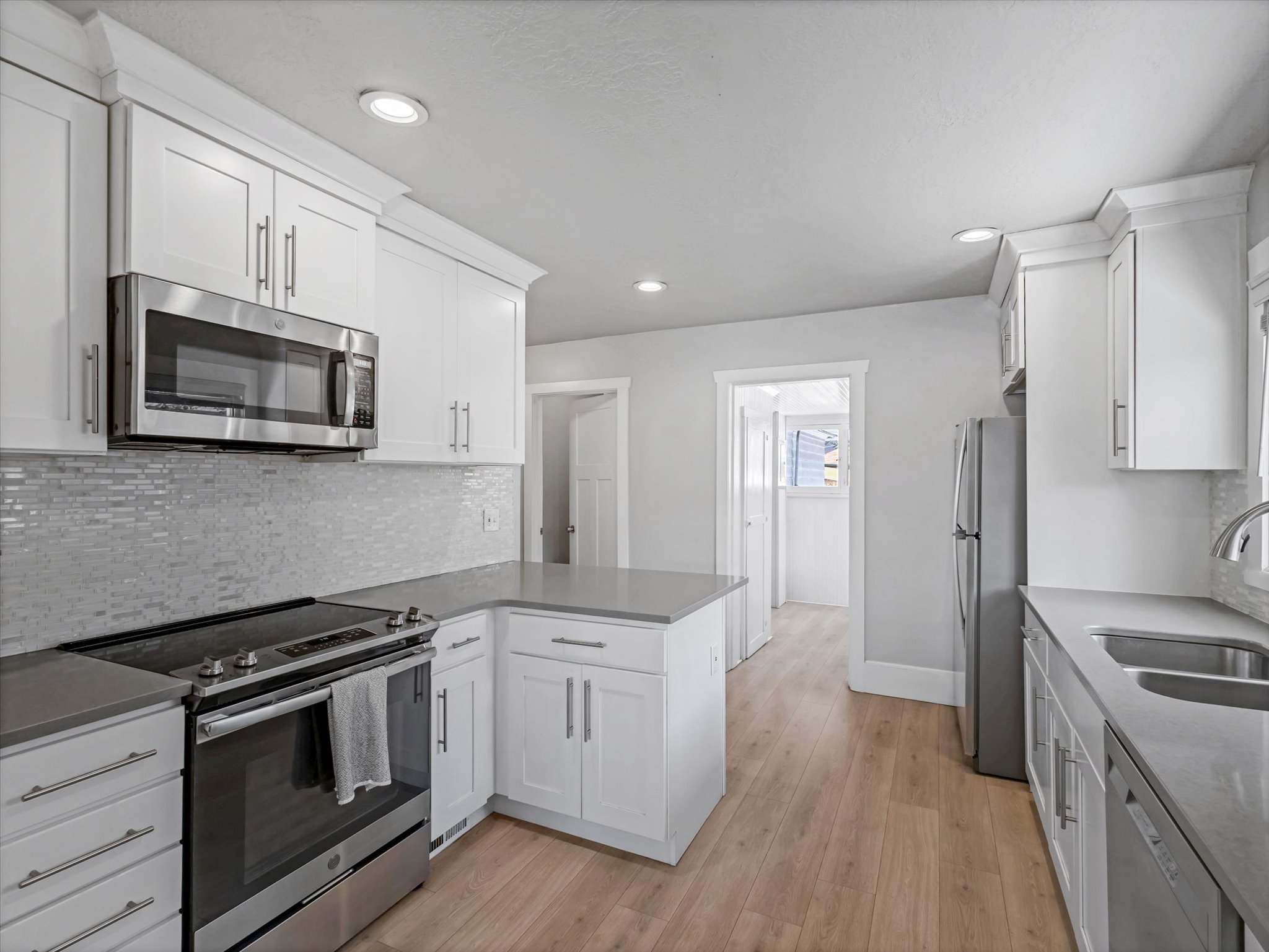 Modern kitchen featuring white shaker cabinetry, stainless steel appliances, light wood-finish flooring, and a mosaic tile backsplash