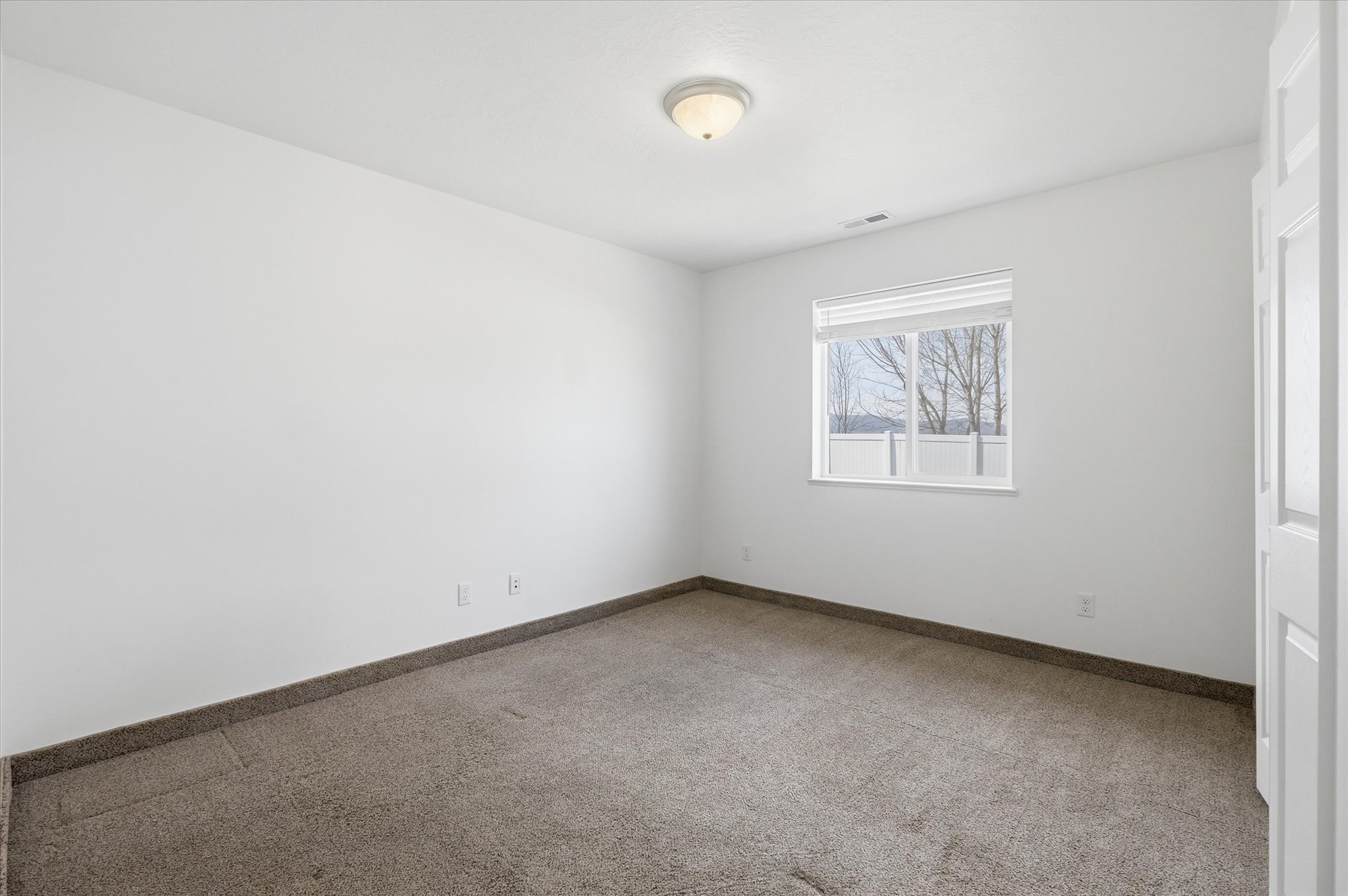 Carpeted room featuring a single window with blinds, white walls, and a ceiling-mounted light fixture