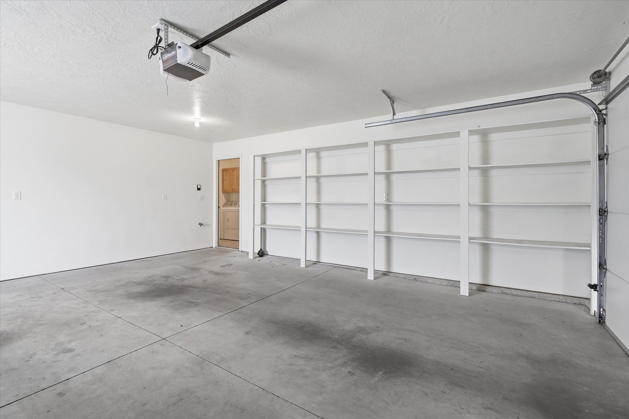 Spacious garage featuring a concrete floor, built-in shelving, an automatic garage door opener, and a service door