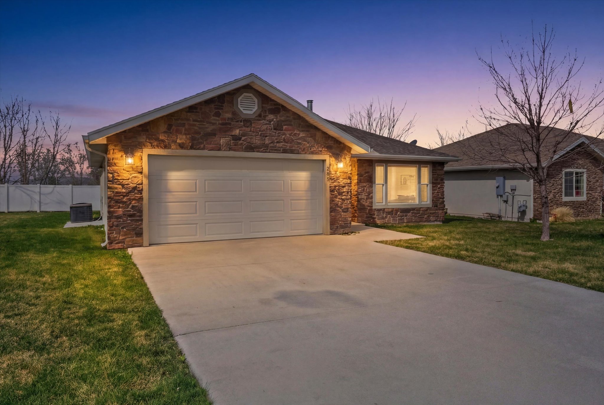 Stone veneer exterior featuring a two-car garage, concrete driveway, and established front lawn