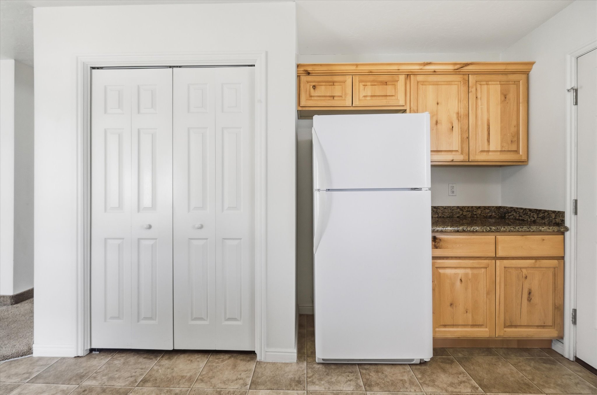 Compact kitchen area featuring wood-finish cabinetry, granite-style countertops, and a white refrigerator