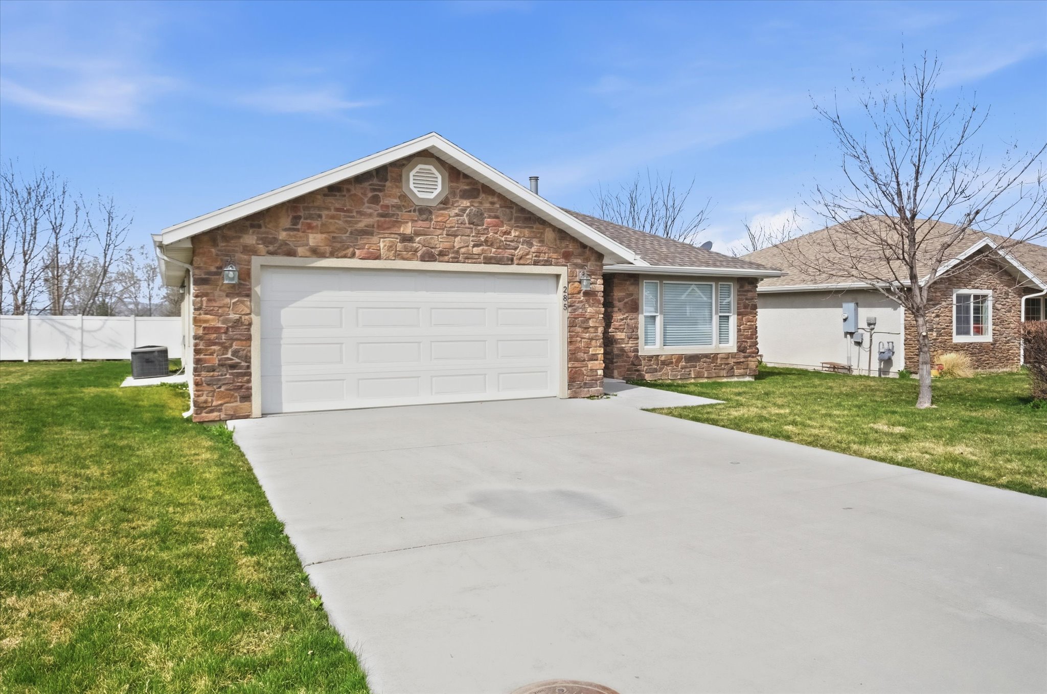 Stone veneer facade with an attached two-car garage, mature landscaping, and a concrete driveway
