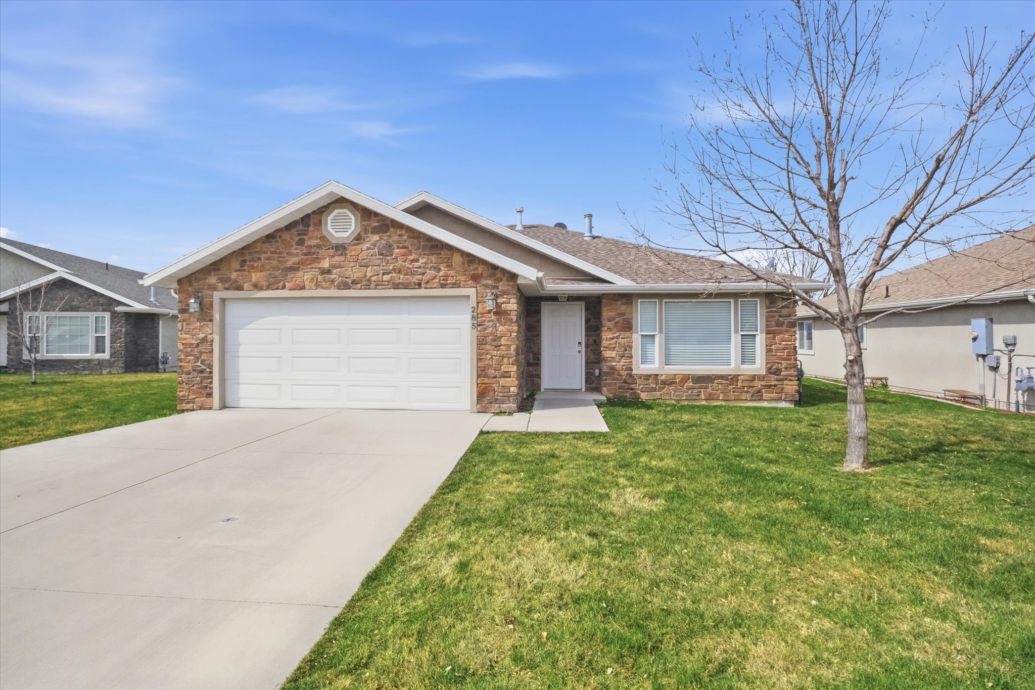 Stone veneer exterior with a two-car garage, concrete driveway, and front lawn