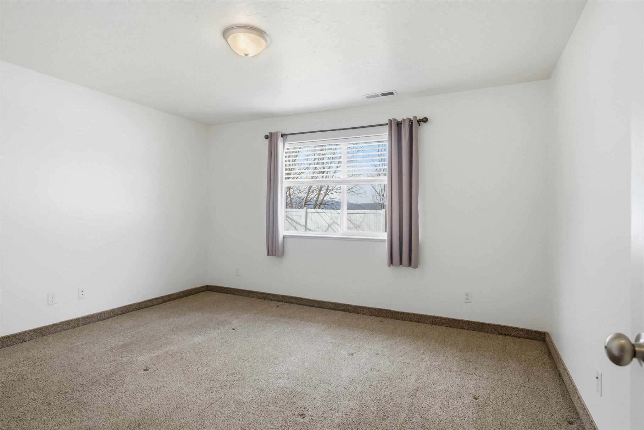 Carpeted interior space featuring a window with white blinds, a simple ceiling light fixture, and white painted walls