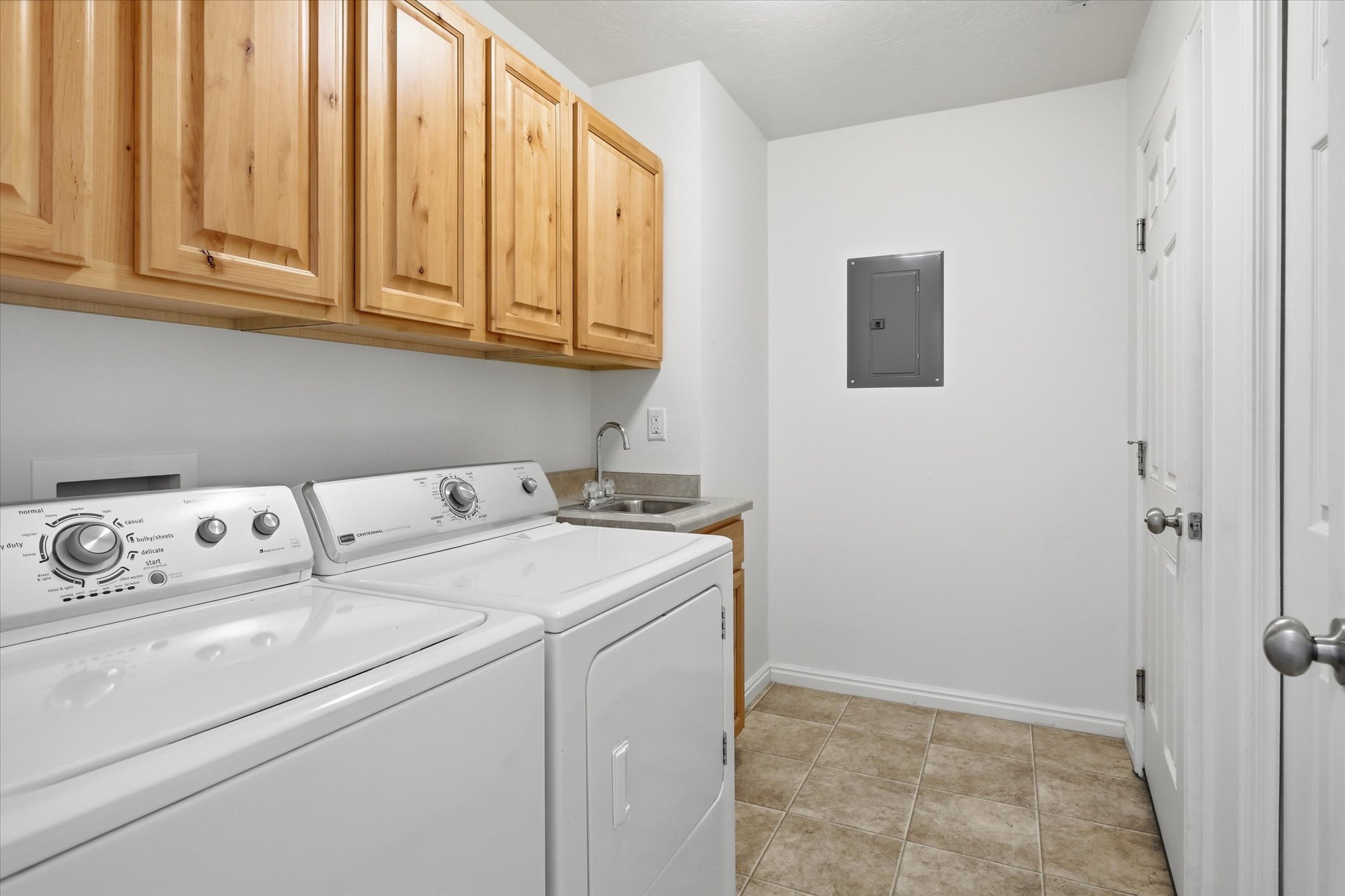 Functional laundry area featuring upper wood cabinetry, a utility sink with a faucet, and tiled flooring