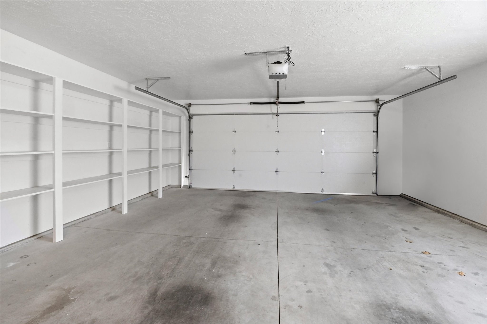 Spacious garage featuring a concrete floor, built-in shelving, an automatic garage door opener, and a white paneled garage door