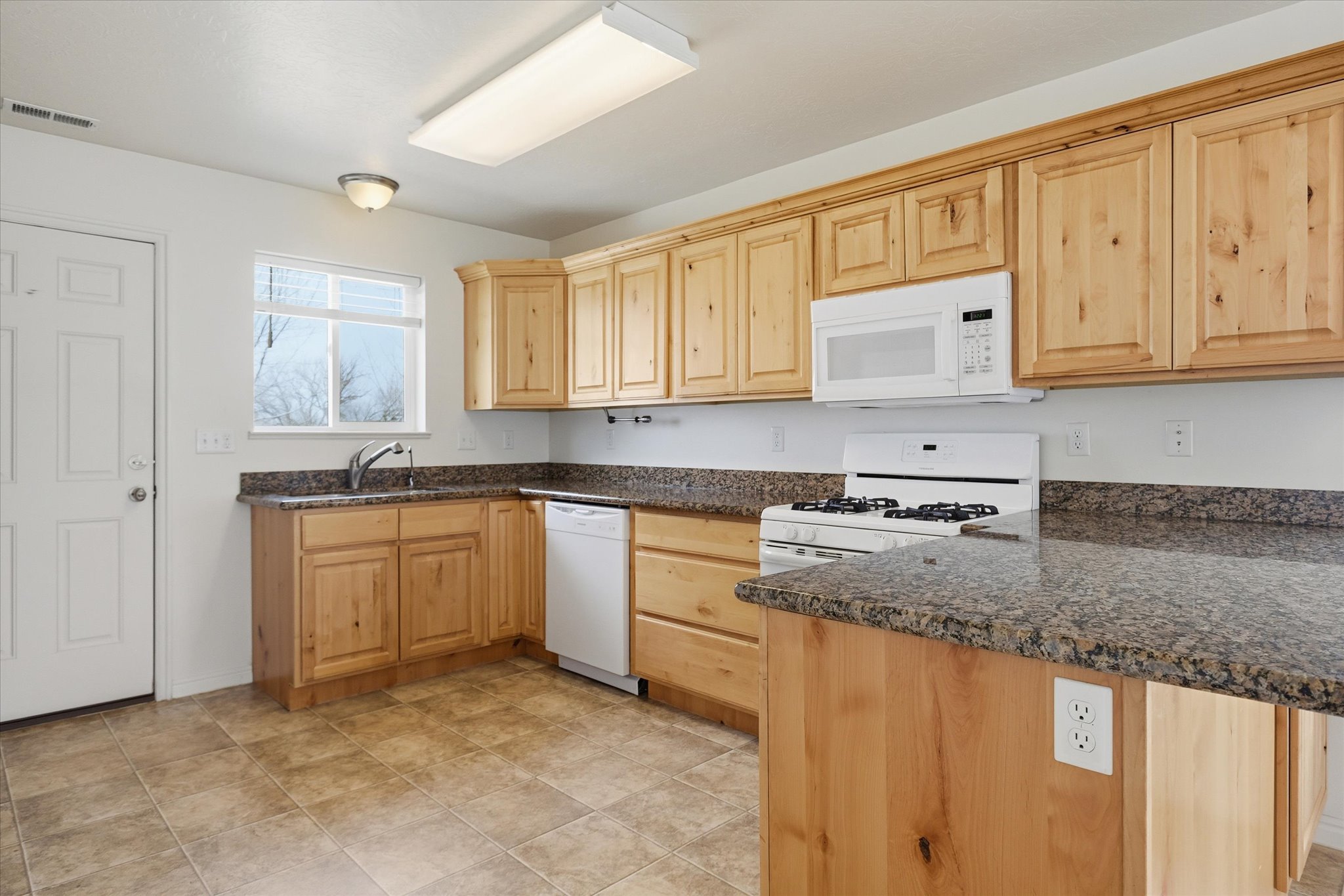 Kitchen featuring natural wood cabinetry, granite-finish countertops, and tile flooring