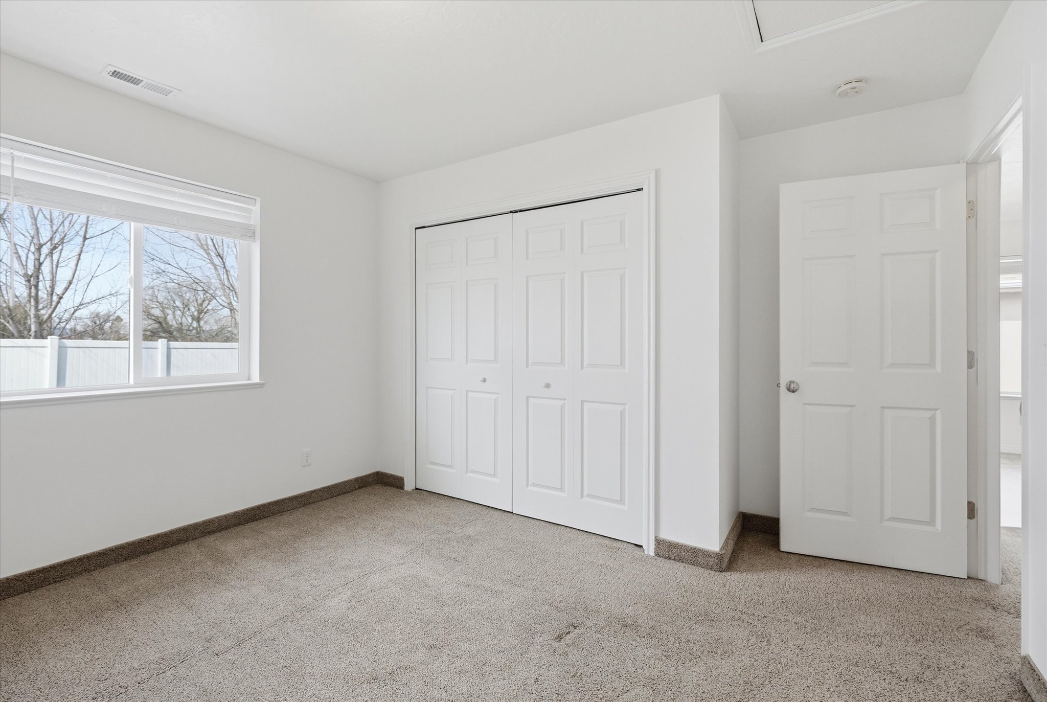 Carpeted room with a white bi-fold closet, a six-panel door, and a horizontal window with blinds