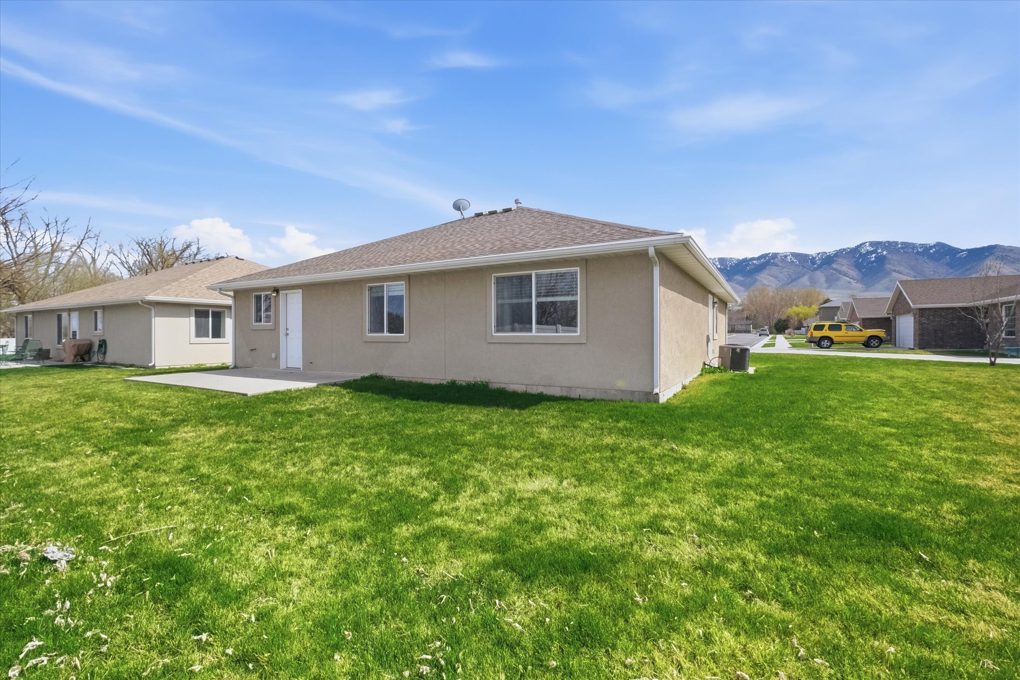 Spacious backyard featuring a manicured lawn, concrete patio, tan stucco exterior, and a mountain backdrop