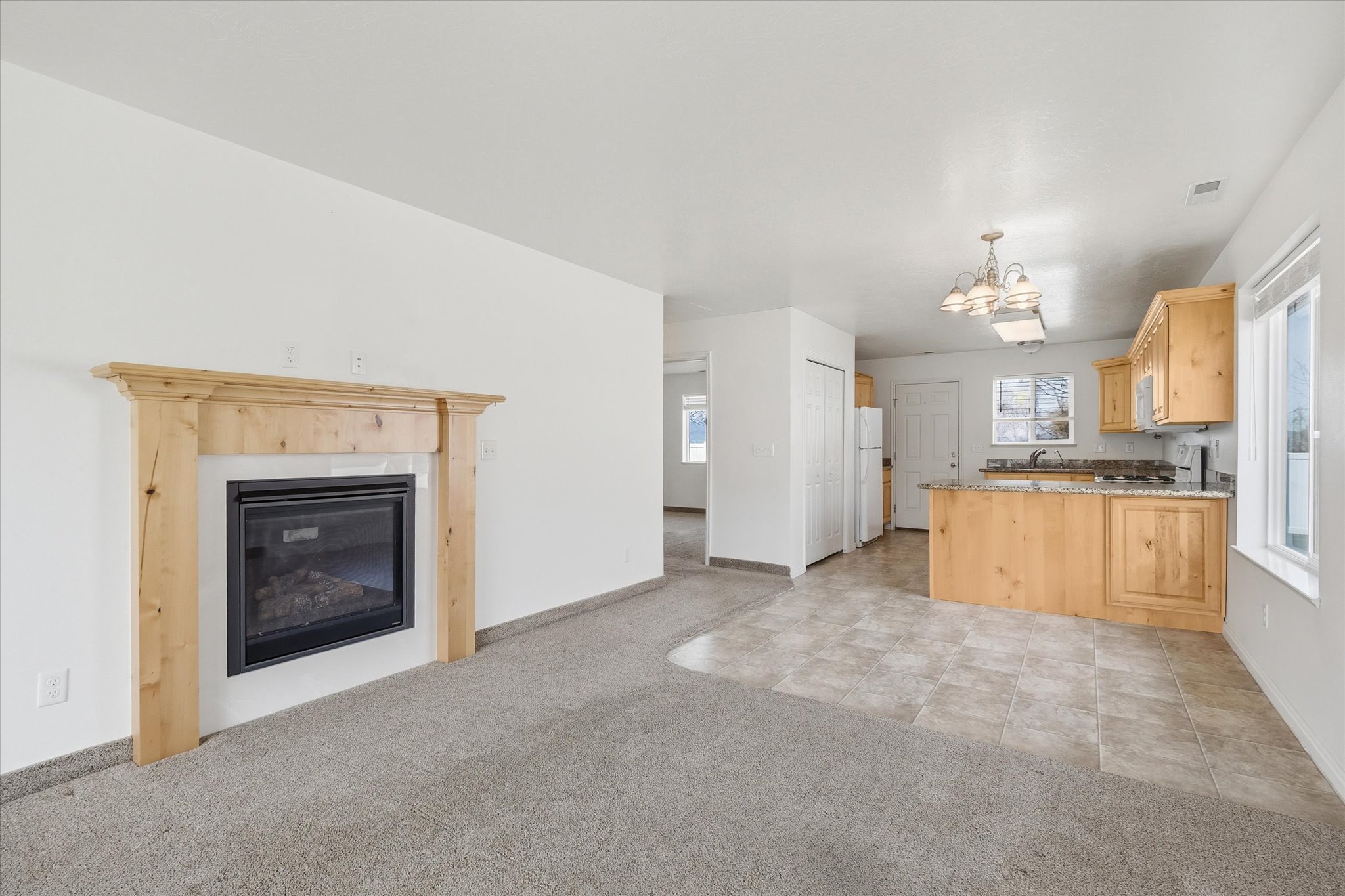 Living area featuring a fireplace with a light wood mantle, light gray carpet, and white walls
