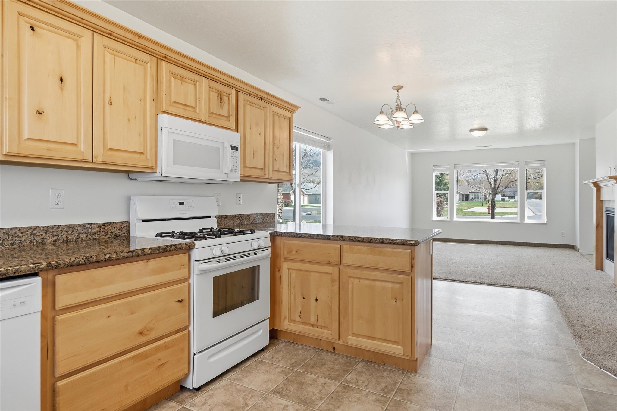 Kitchen featuring natural wood cabinetry, white appliances, and speckled countertops