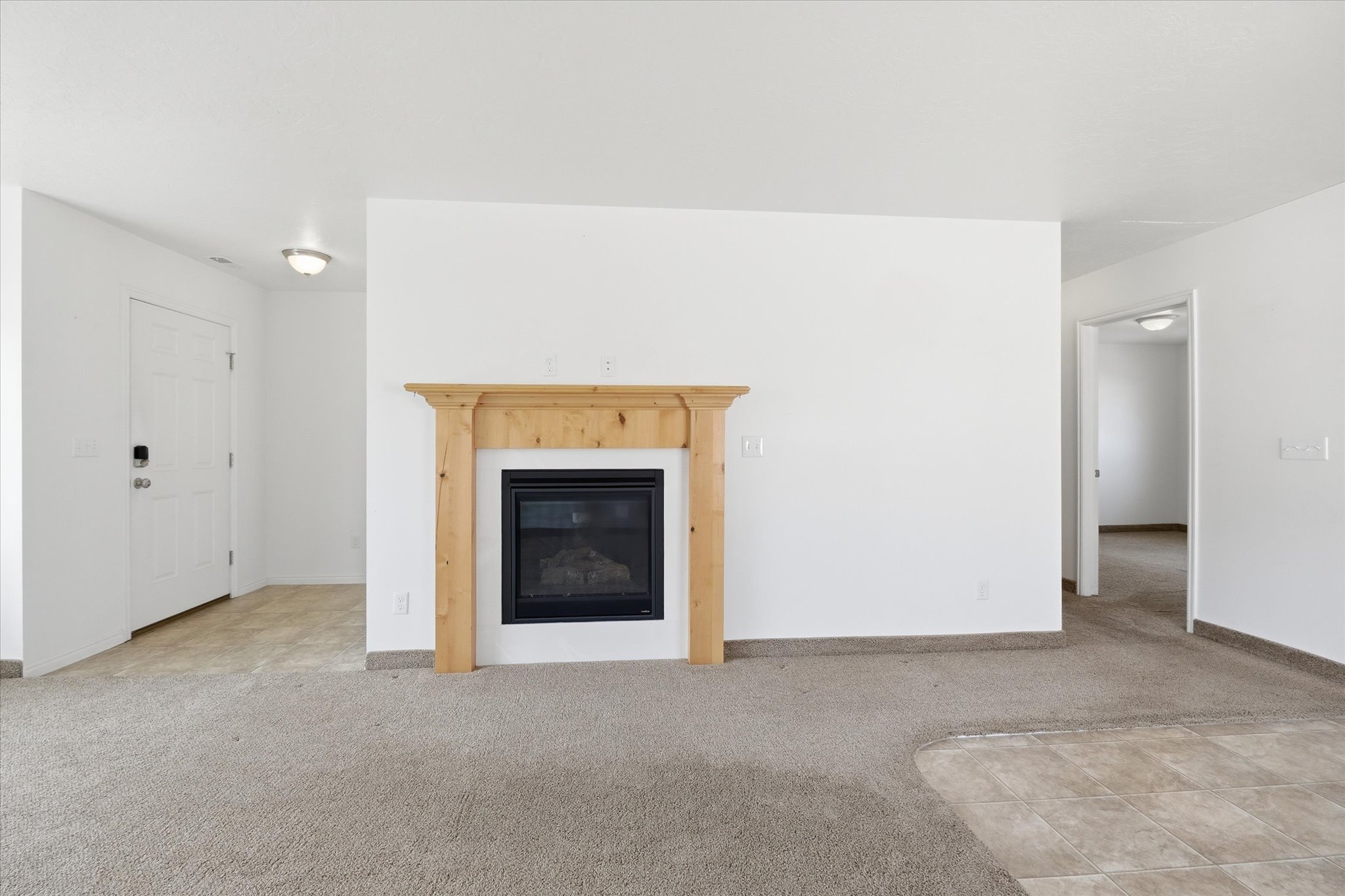 Living area featuring a gas fireplace with a natural wood mantel, light-toned carpet, and a tiled entry