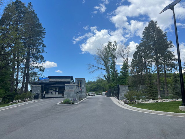 Gated entry with stone pillars, mature trees, asphalt paving, and a security gate
