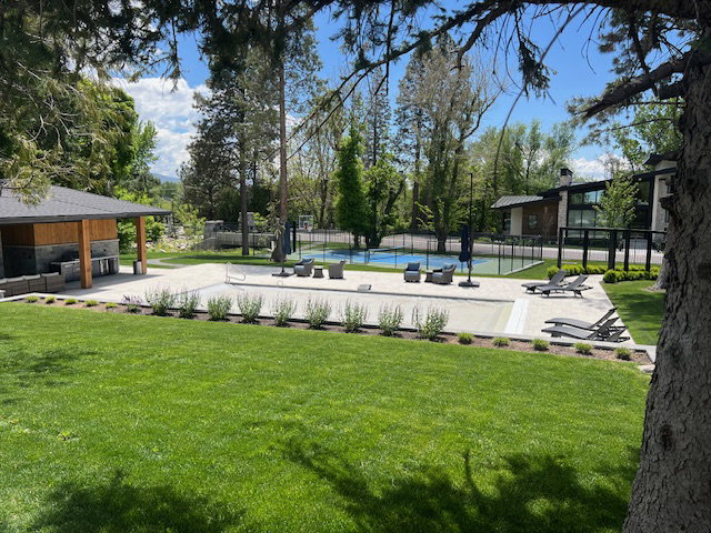 Expansive backyard featuring a manicured lawn, an outdoor kitchen with integrated appliances, a covered patio area, a swimming pool with a cover, and an adjacent sports court