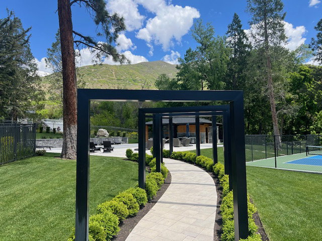 Paved pathway lined with manicured hedges and a modern pergola structure leading to outdoor amenity areas