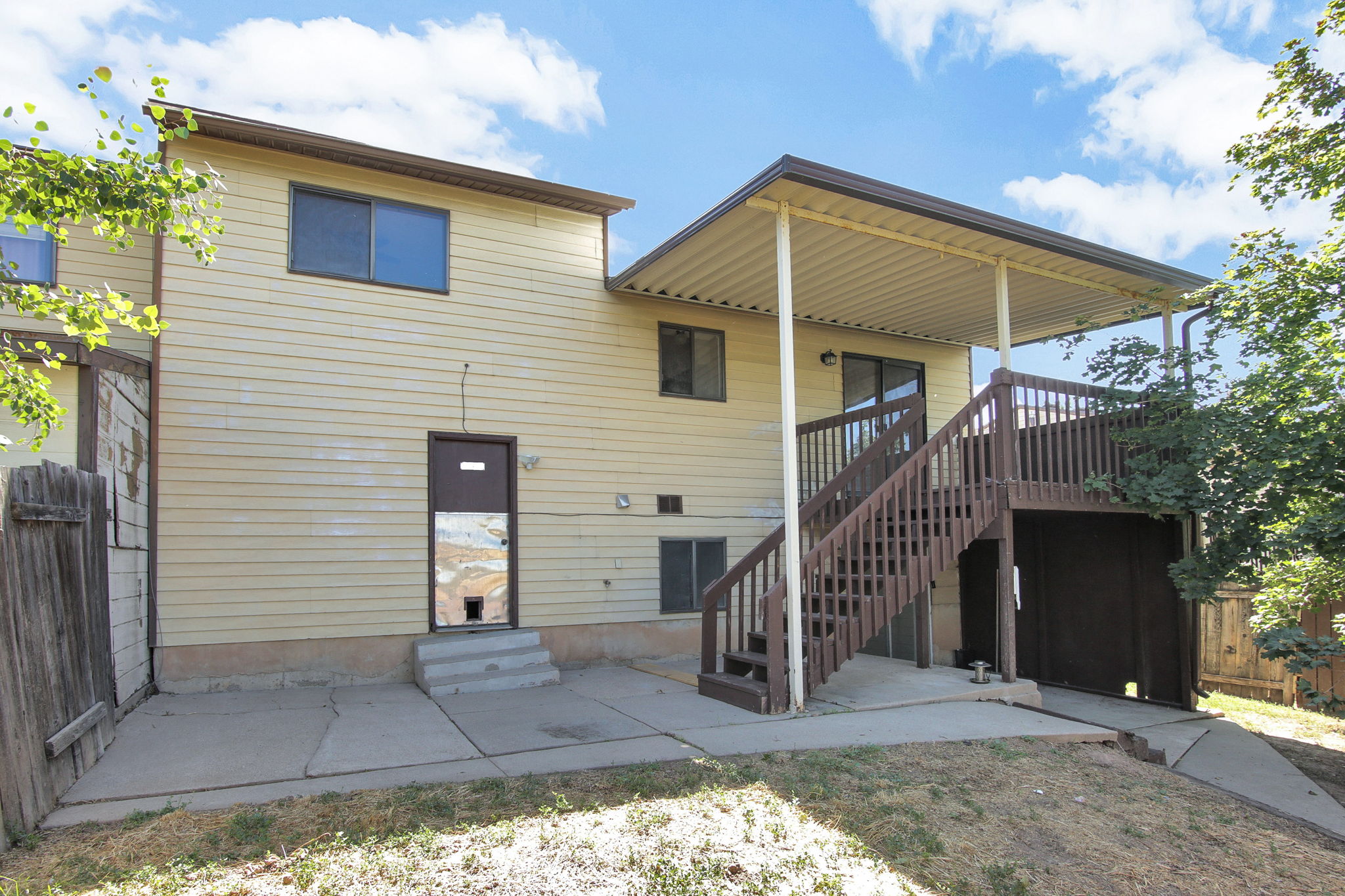 Rear exterior featuring a covered deck with a complete staircase, ground-level patio, and horizontal siding