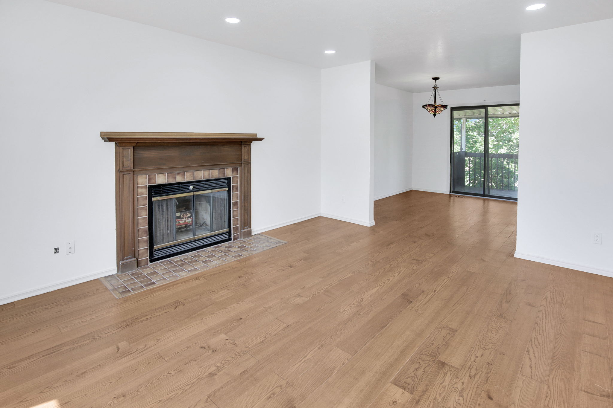 Spacious interior featuring wood-finish flooring, a fireplace with a wood mantel and brick surround, recessed lighting, and a sliding glass door leading to an outdoor balcony