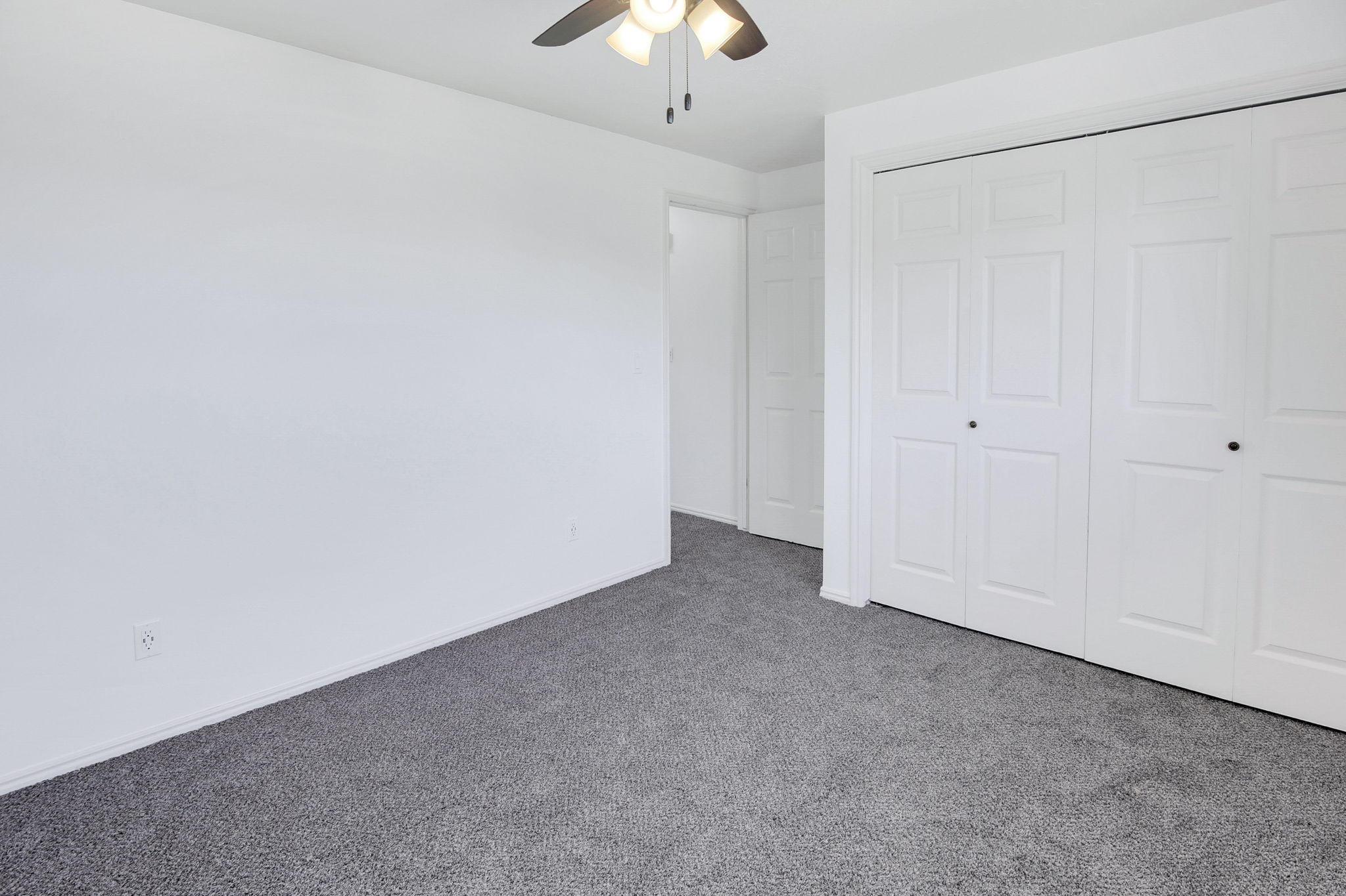 Room featuring gray carpeting, white walls, white bifold closet doors, and an overhead ceiling fan with lighting