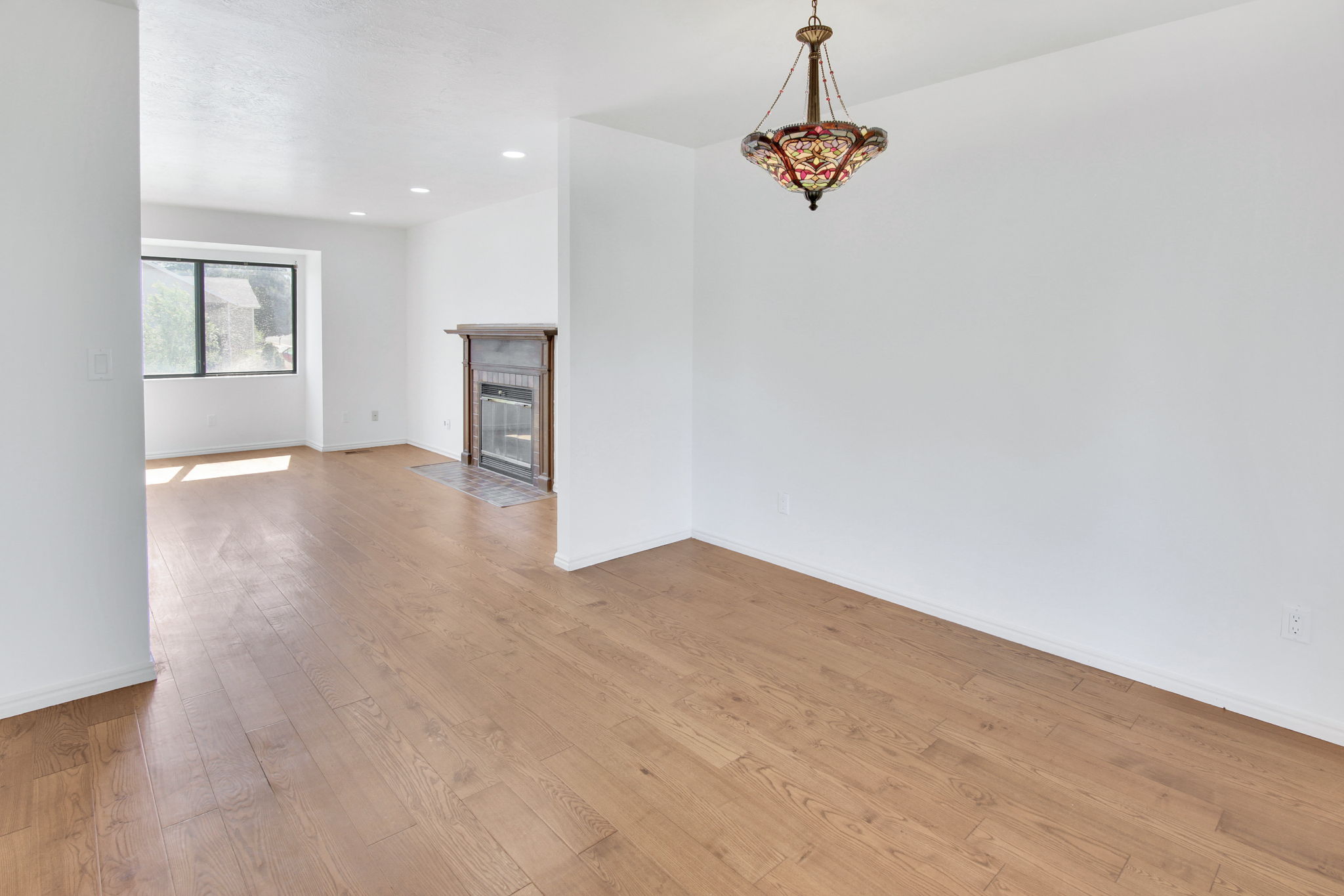 Spacious interior featuring wood-finish flooring, a decorative chandelier, recessed lighting, a fireplace with a tile hearth, and a large window