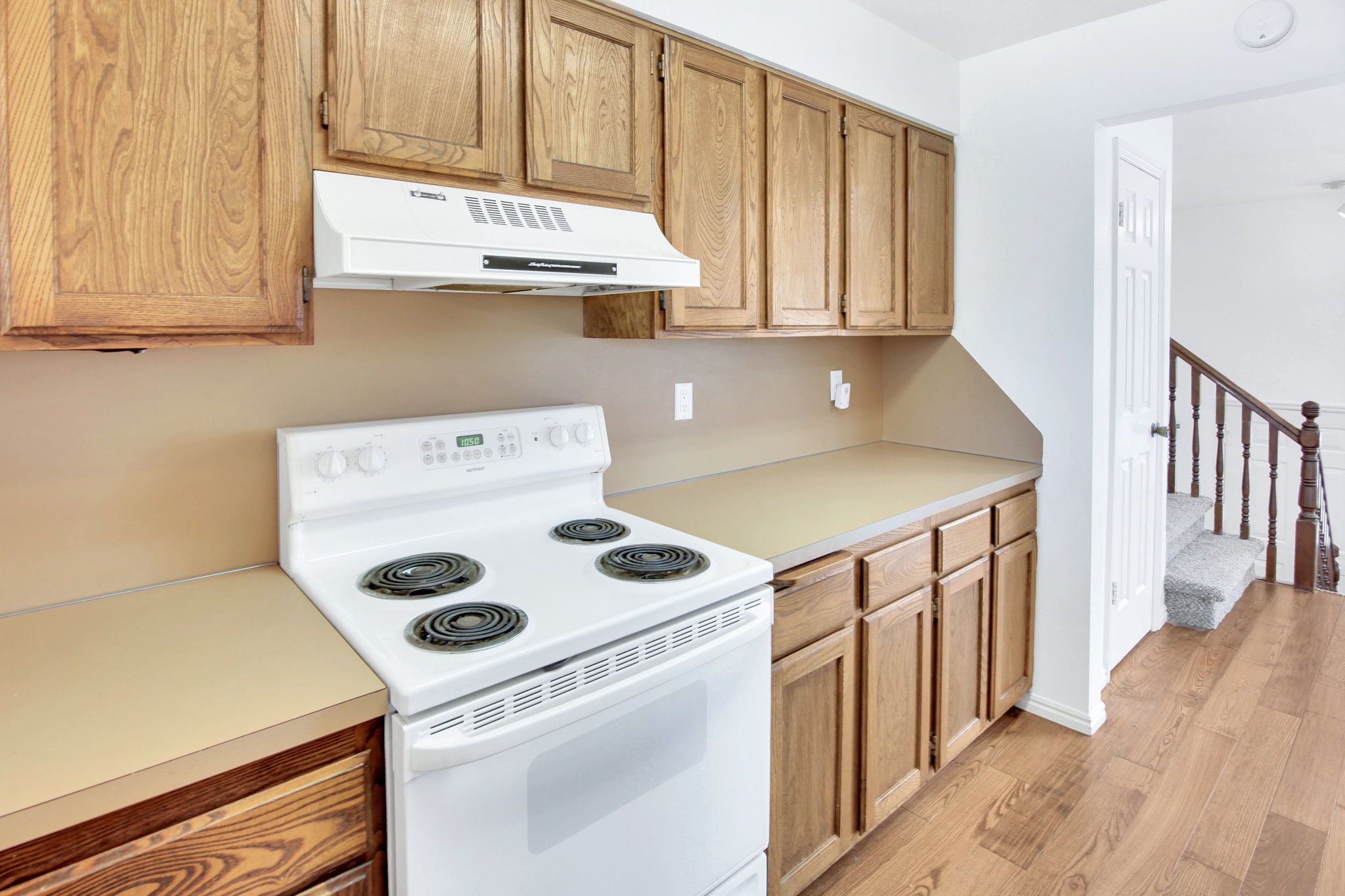 Kitchen featuring wood-finish cabinetry, light-toned countertops, and a white electric range with matching range hood