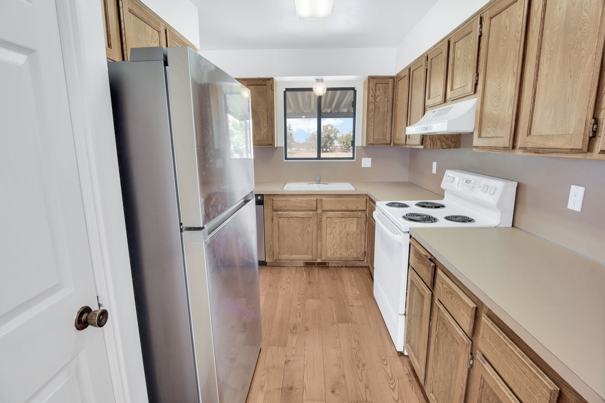 Kitchen featuring wood-finish cabinetry, neutral countertops, a white electric range, and wood-finish flooring