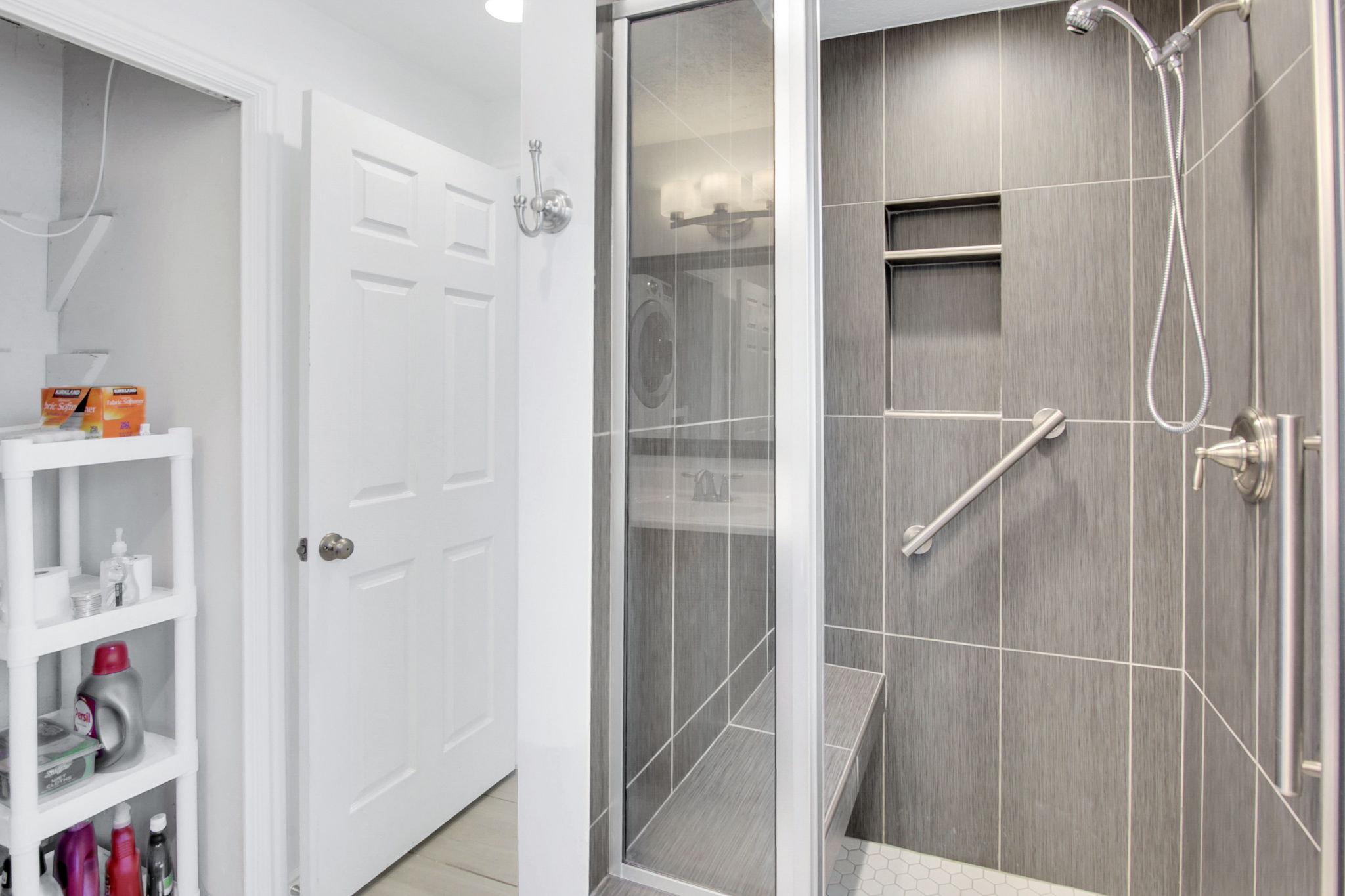 Glass-enclosed shower featuring large format gray wall tiling, built-in shelving, an integrated bench, and a brushed nickel shower fixture