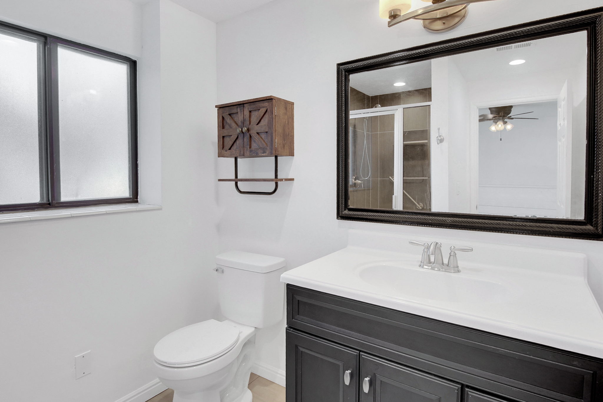 Bathroom featuring a dark wood vanity with a white countertop and integrated sink, a framed mirror, and a wall-mounted light fixture