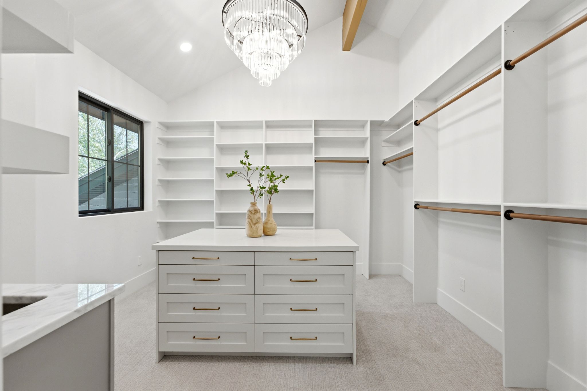 Custom closet system featuring extensive shelving, hanging rods, central island with drawers, vaulted ceiling, and a prominent chandelier