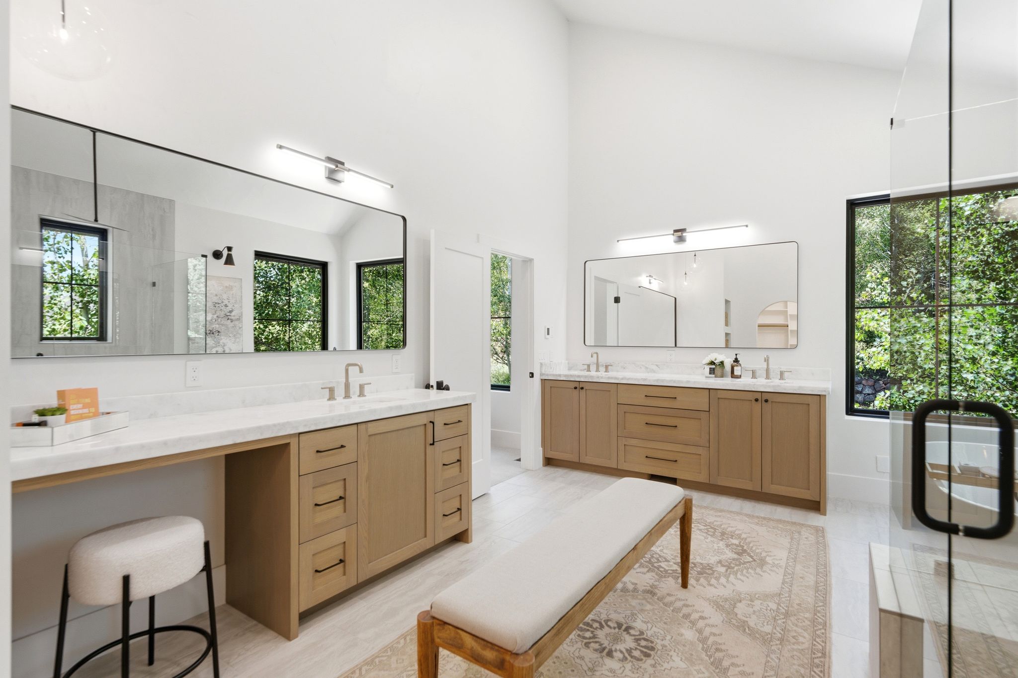 Spacious bathroom featuring twin wood-finish vanities with marble-look countertops and integrated sinks, large rectangular mirrors, and a glass-enclosed shower with black-framed windows