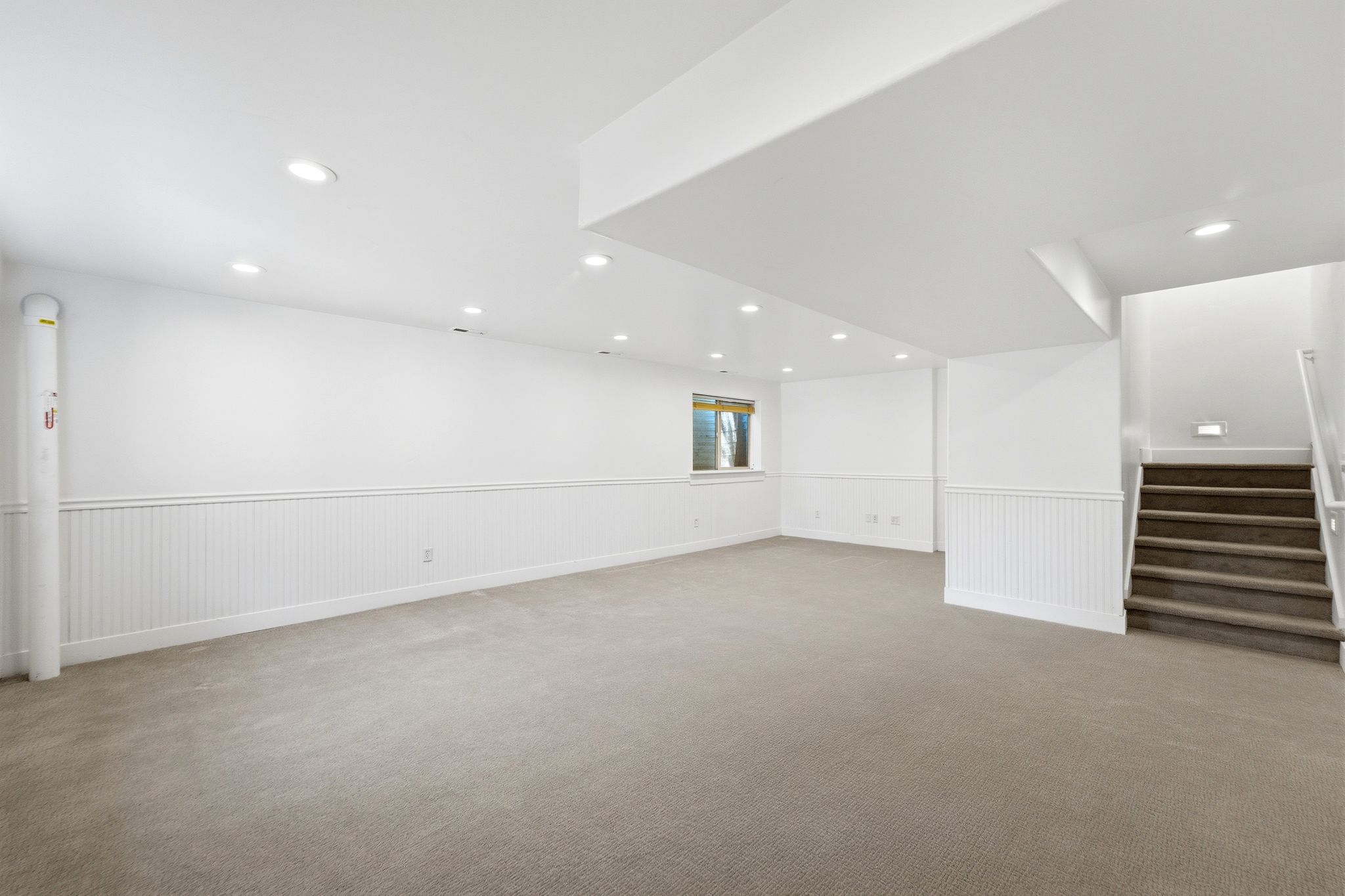 Spacious lower-level room featuring recessed lighting, light carpeting, and white beadboard wainscoting