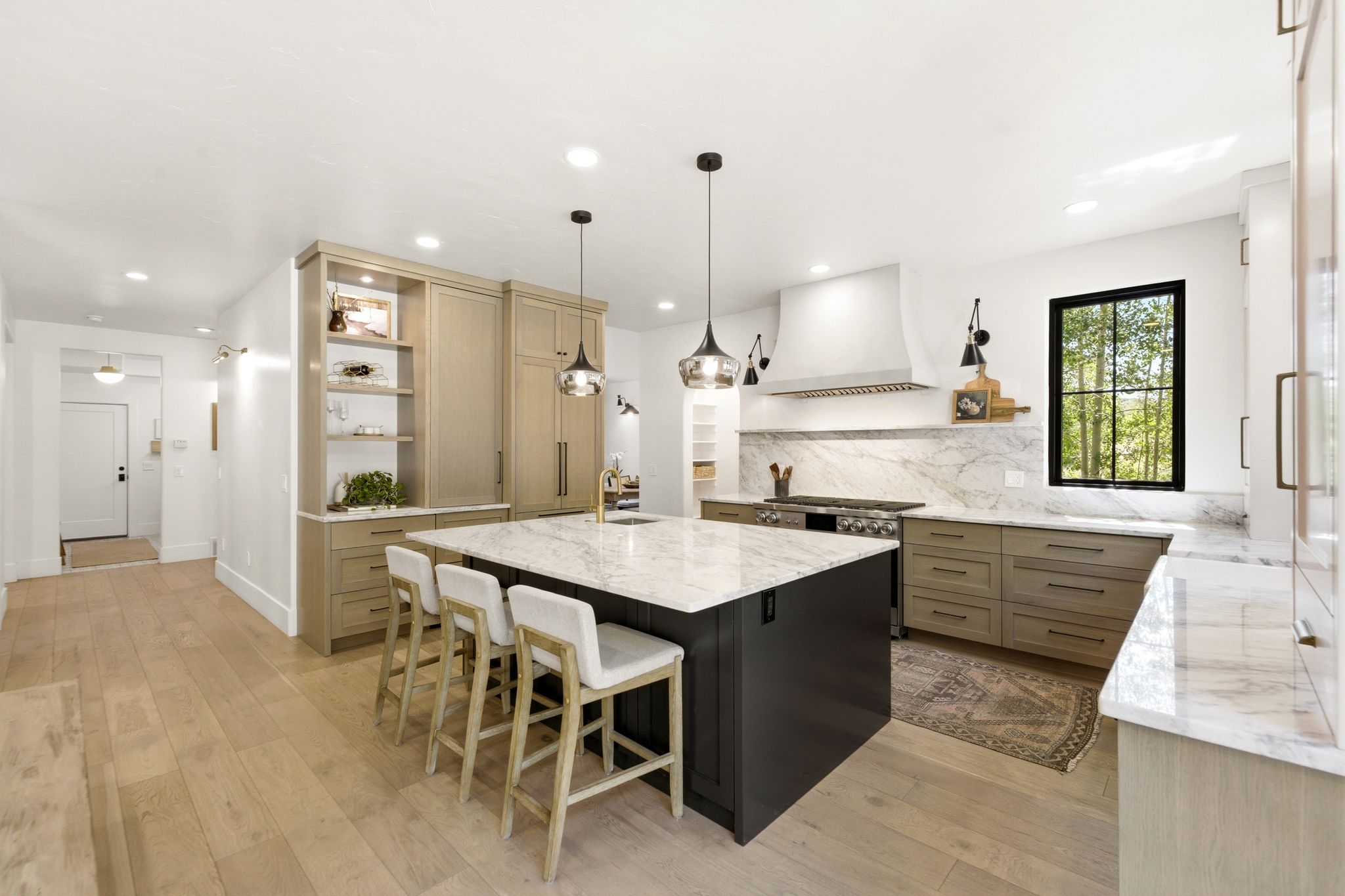 Gourmet kitchen featuring a large central island with seating, integrated appliances, natural wood-finish flooring, a contemporary range hood, and a striking black-framed window
