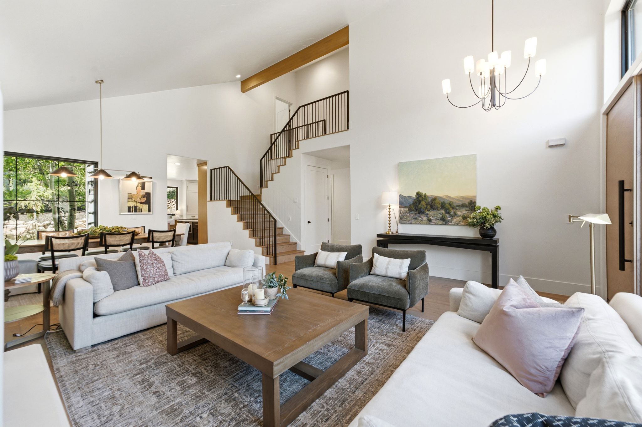 Vaulted ceiling living area featuring wood-finish flooring, a contemporary chandelier, and a prominent staircase with black metal railings