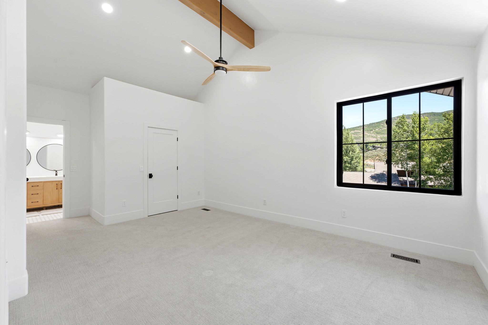 Spacious room featuring vaulted ceilings, a prominent exposed wood beam, and a contemporary ceiling fan