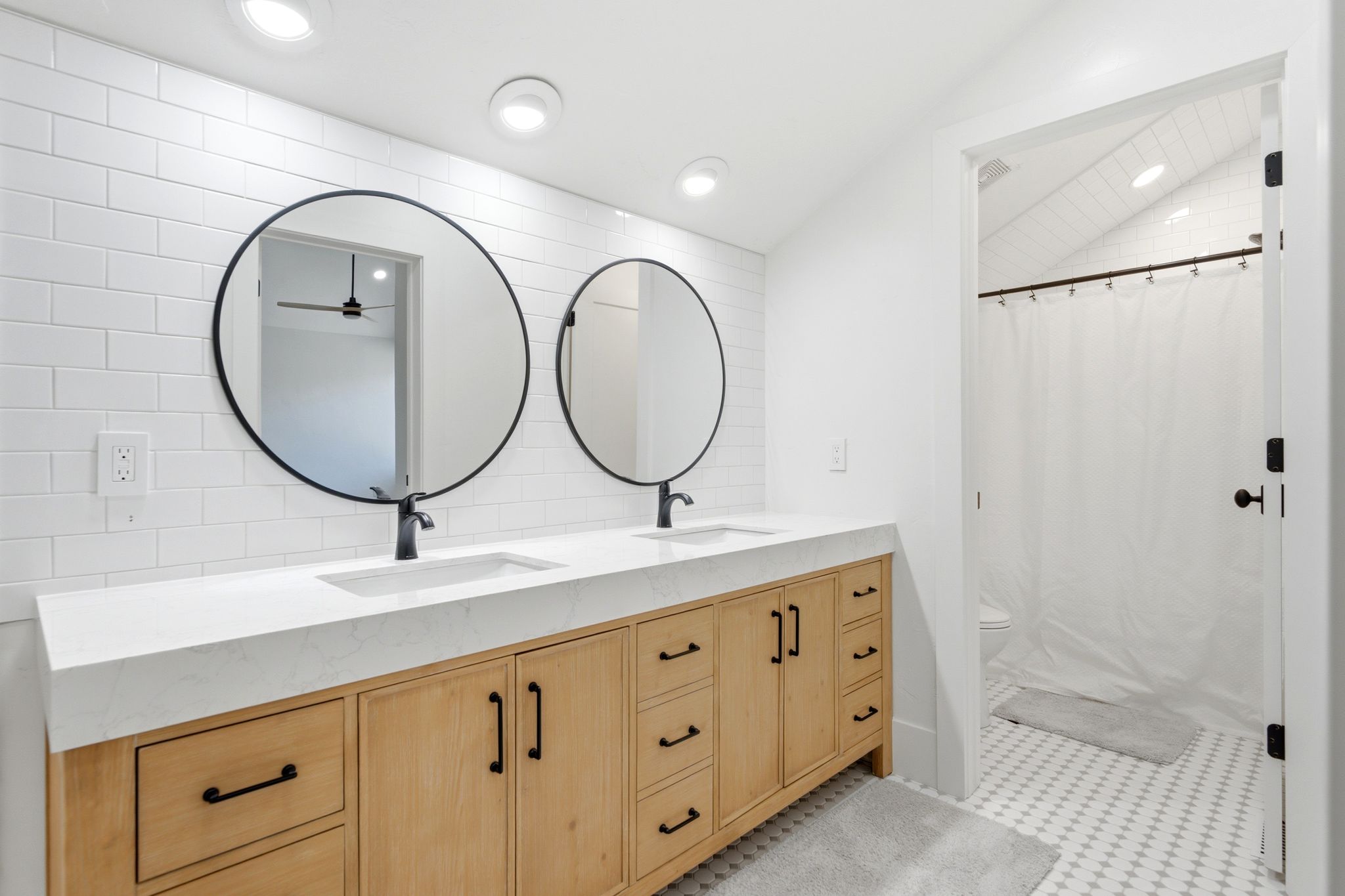 Double vanity featuring wood-finish cabinetry, white countertops, and matte black hardware